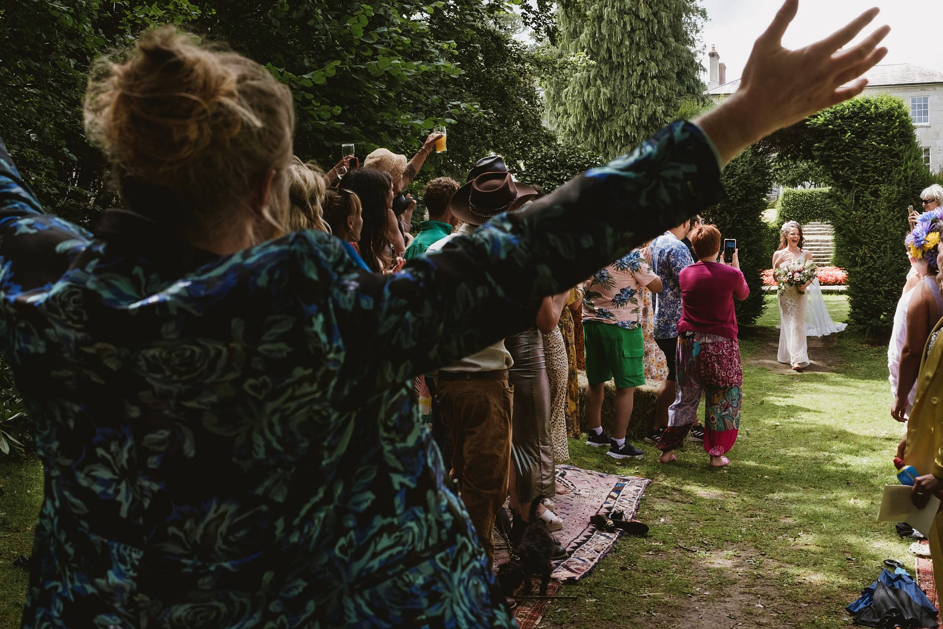 Bride walking down outdoor aisle, people cheering.