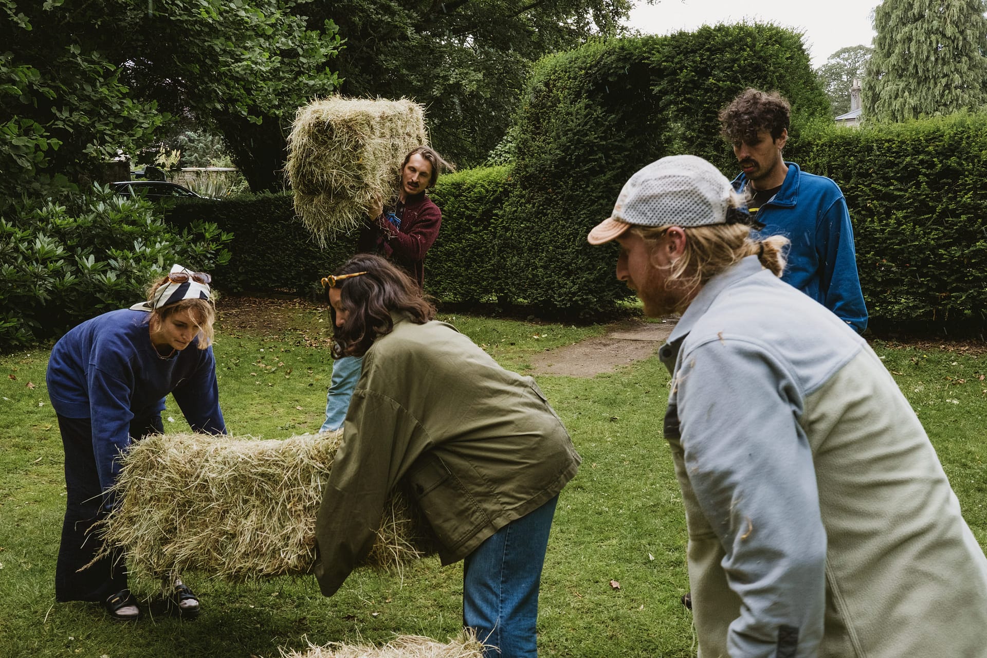 People working together carrying hay bales outside.