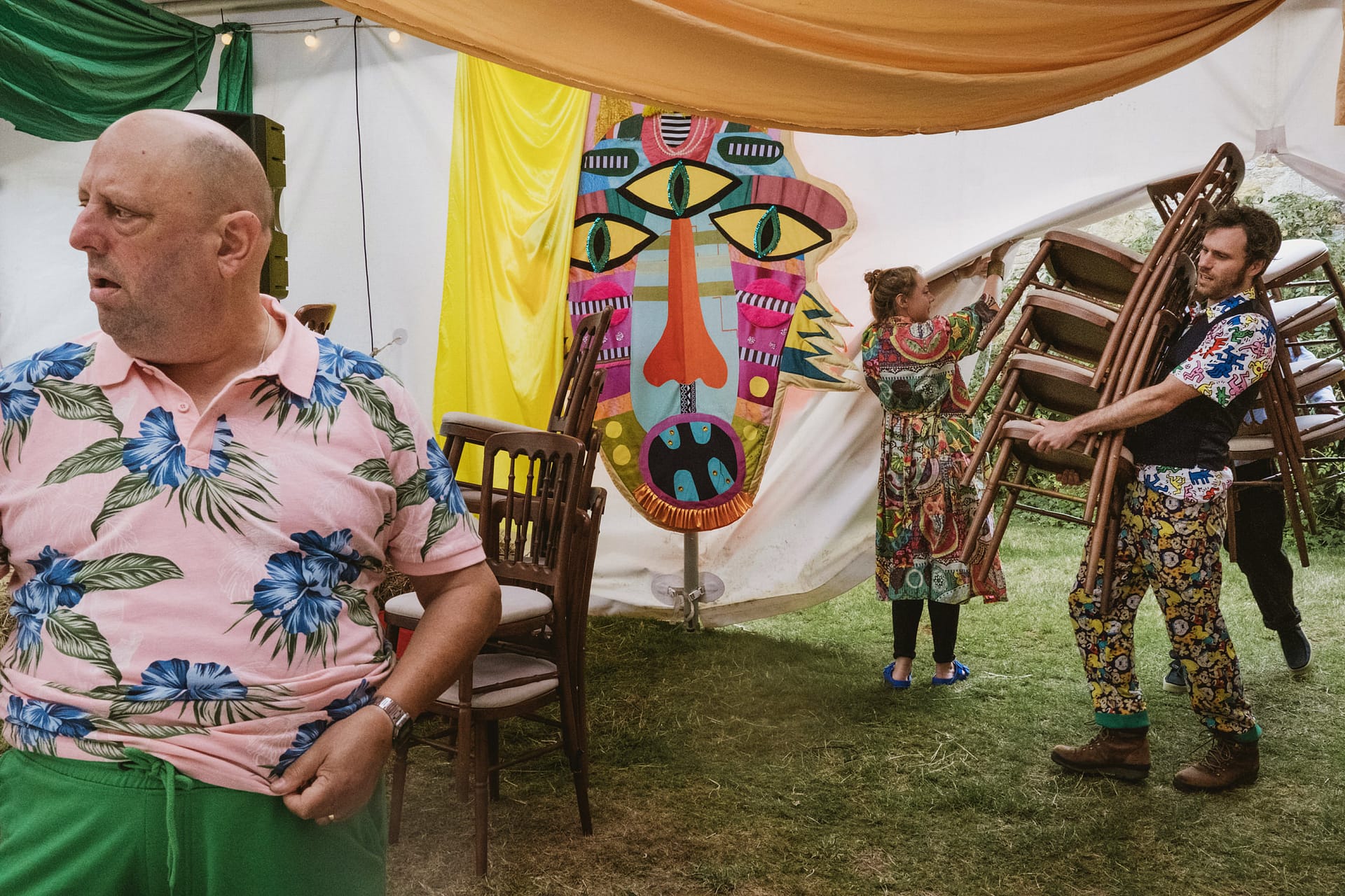 Colourful festival, people moving chairs inside decorated tent.