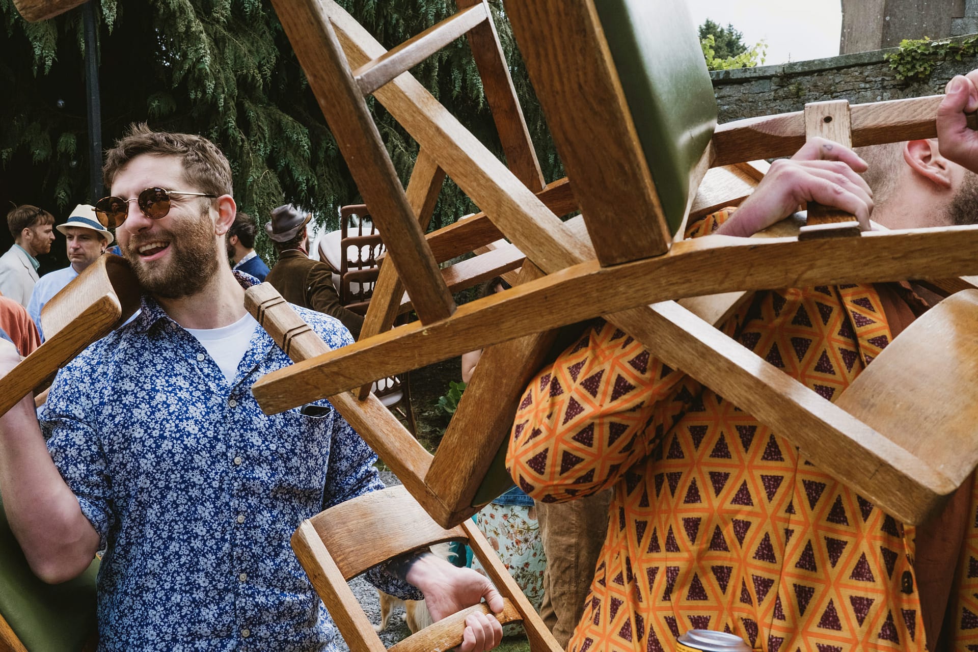 People carrying wooden chairs outdoors.