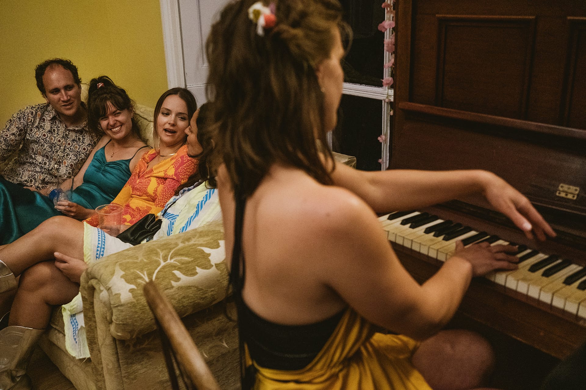 Group of people, one playing piano, others sitting.