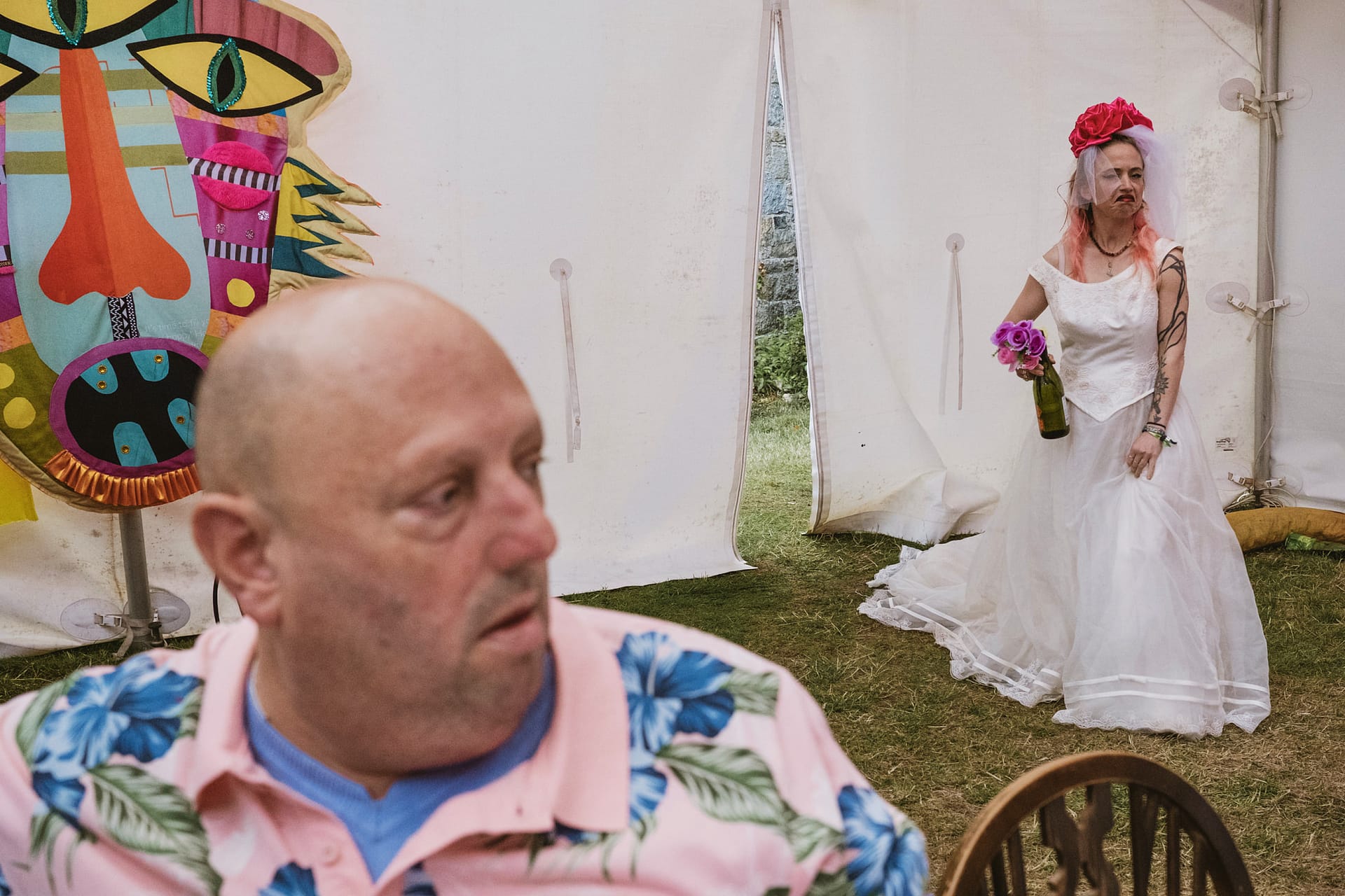Bride with bottle stands behind seated man.