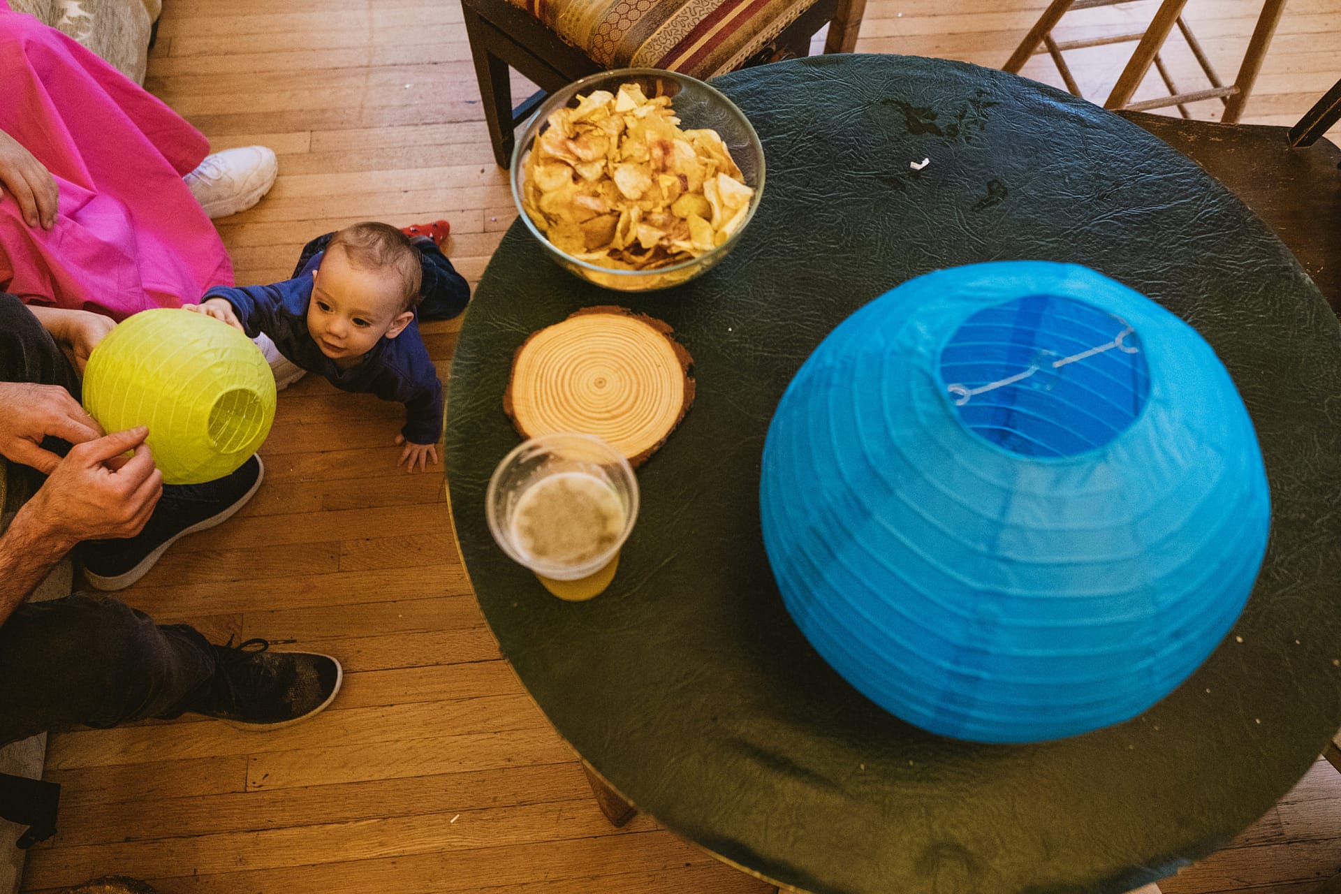 Baby playing with paper lamps, snacks on table.