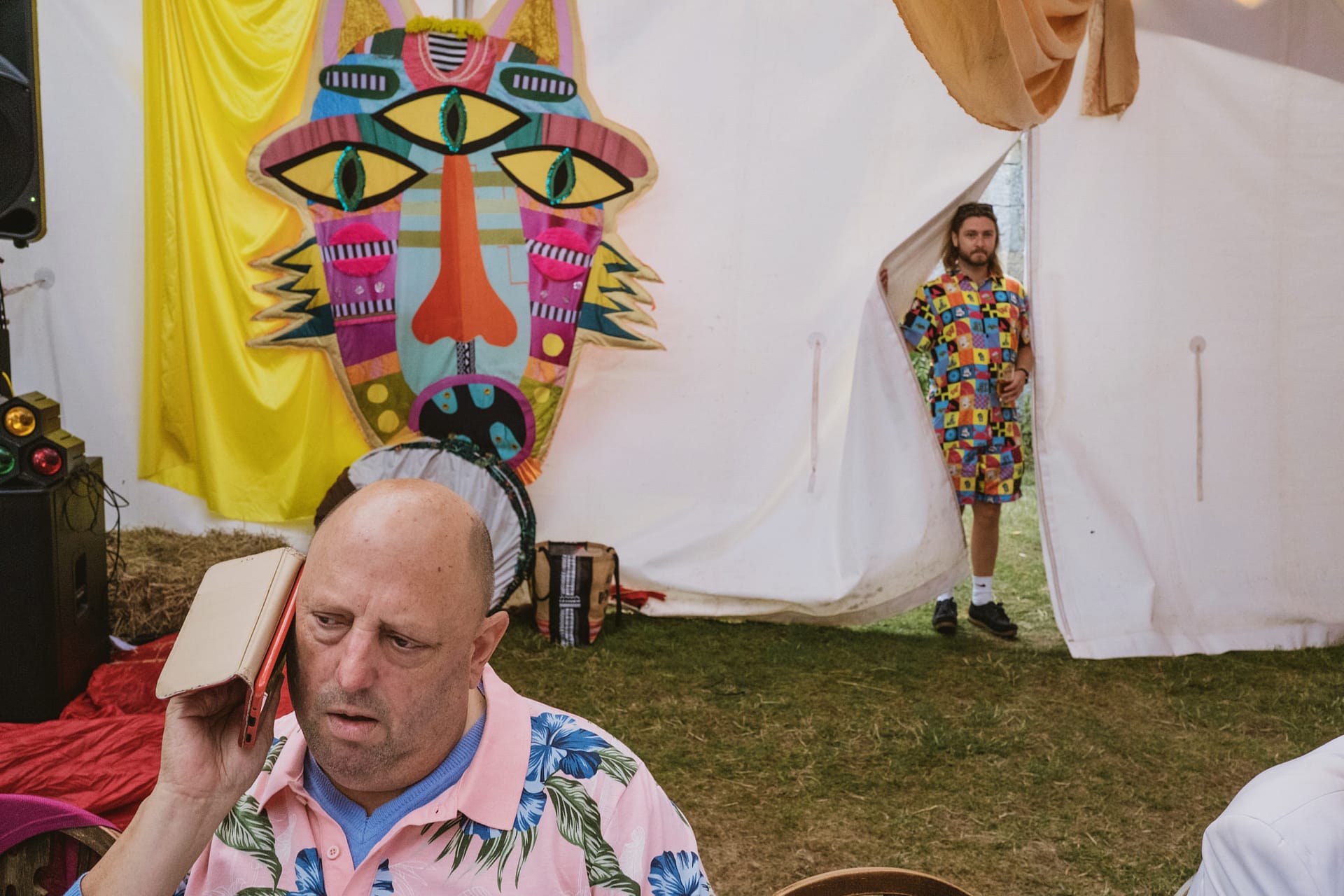 Man on phone, colourful art and person in background.