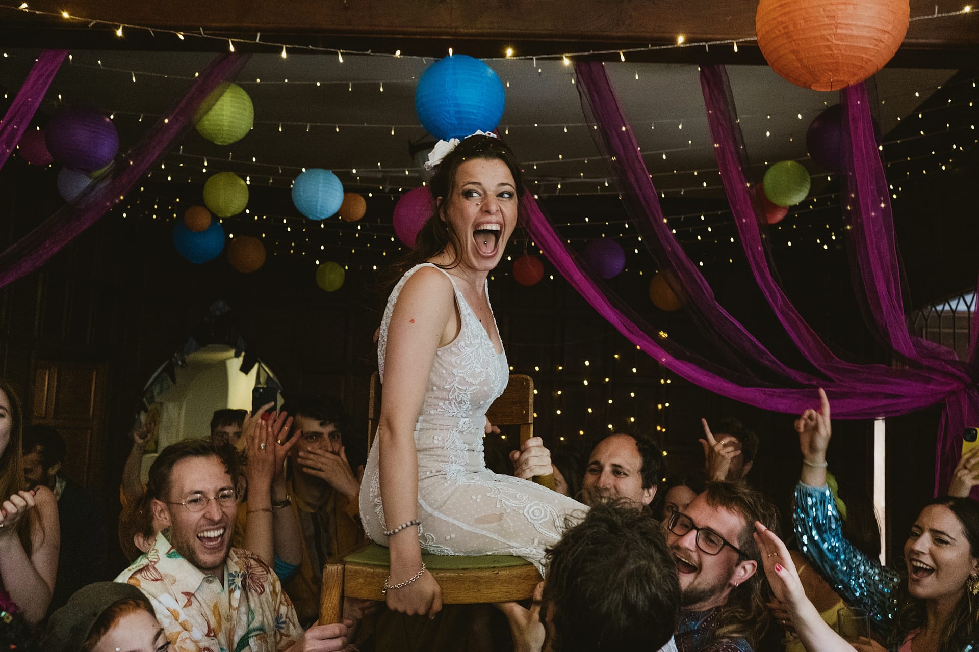 Bride being lifted on chair during festive celebration.