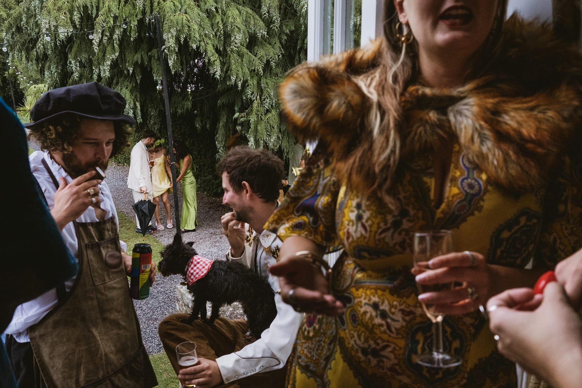 People socialising at outdoor event with drinks and a dog.