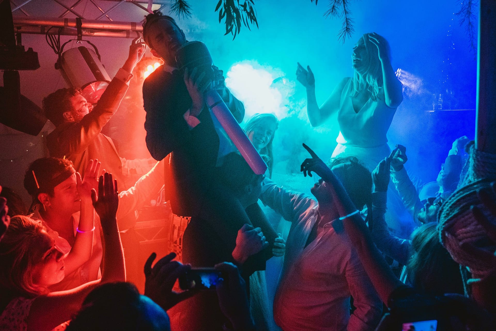 documentary wedding photographer catches the dance floor as the bride and groom ride the shoulders of guests and the colours of light perfectly separate around them