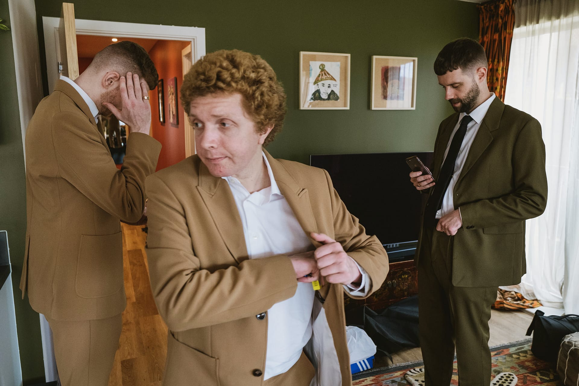 Three men in suits indoors, adjusting jackets.