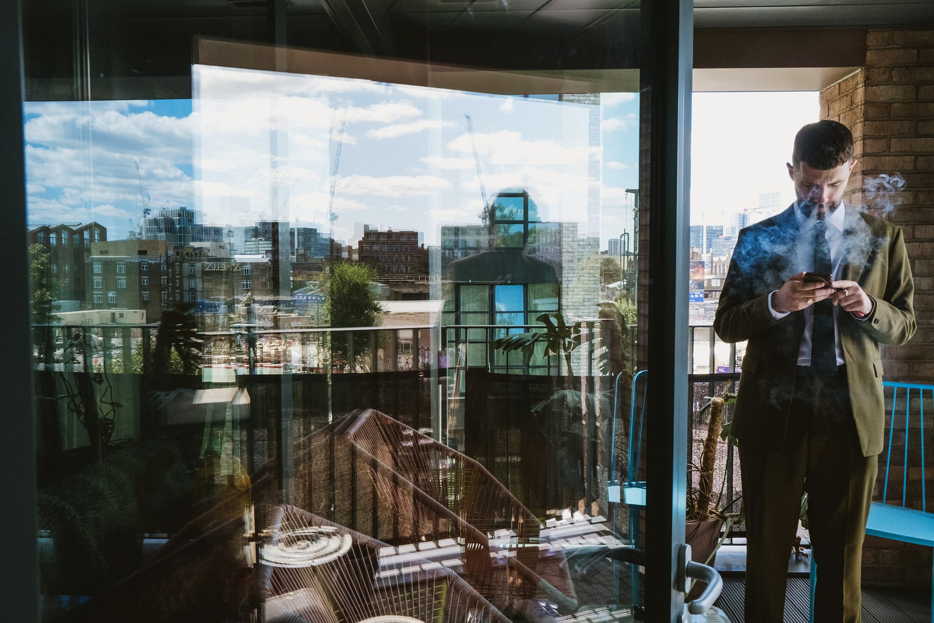 Man smoking on balcony with city view reflection.
