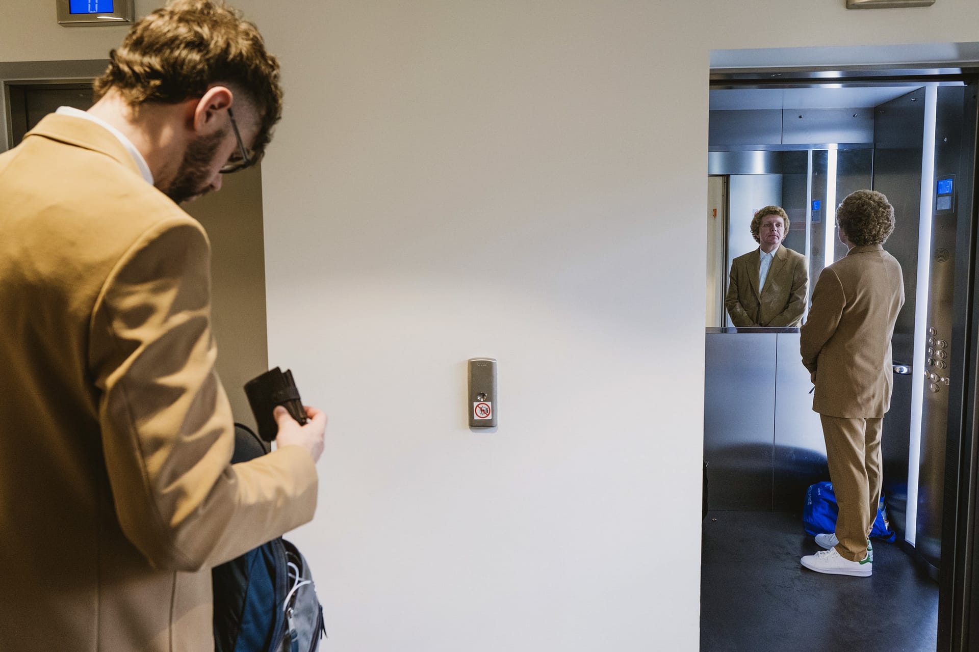 Two men in brown suits by an elevator.
