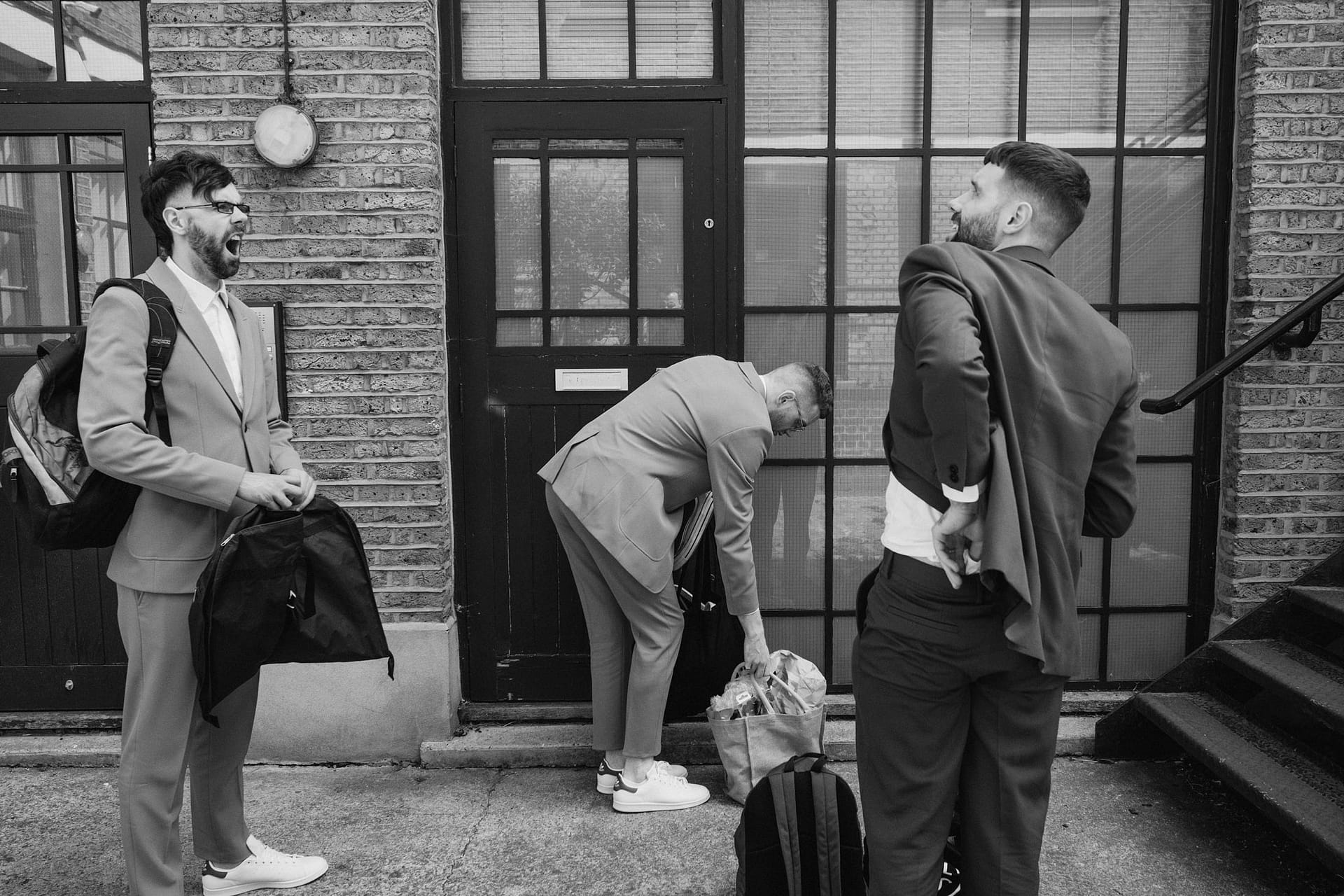 Three men in suits outside a building, one yawning.