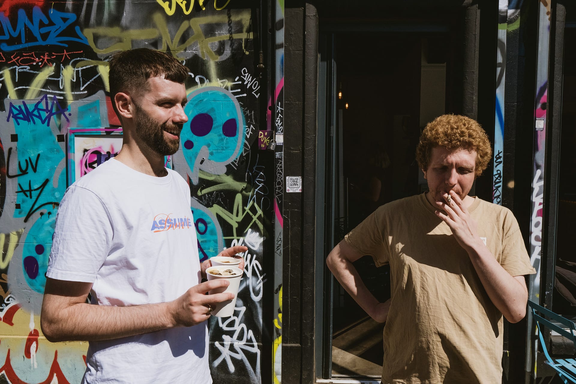 Two men standing near graffiti-covered wall.