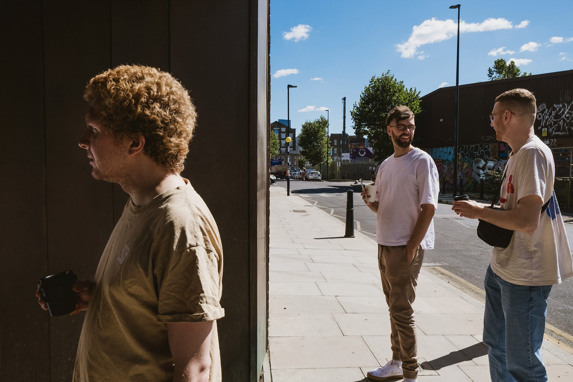 Three men talking and drinking on a sunny street.