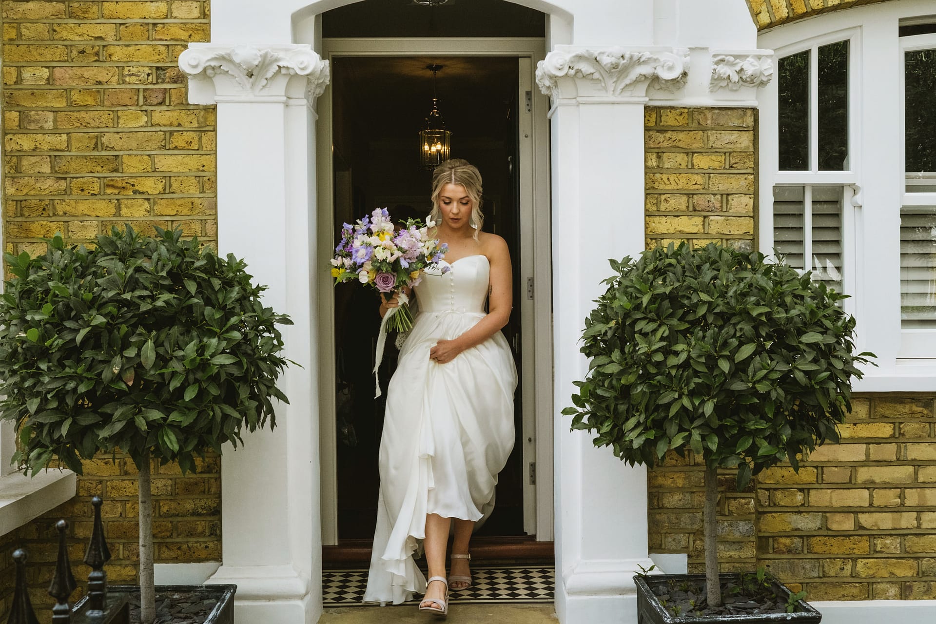 Bride holding bouquet, stepping from house.