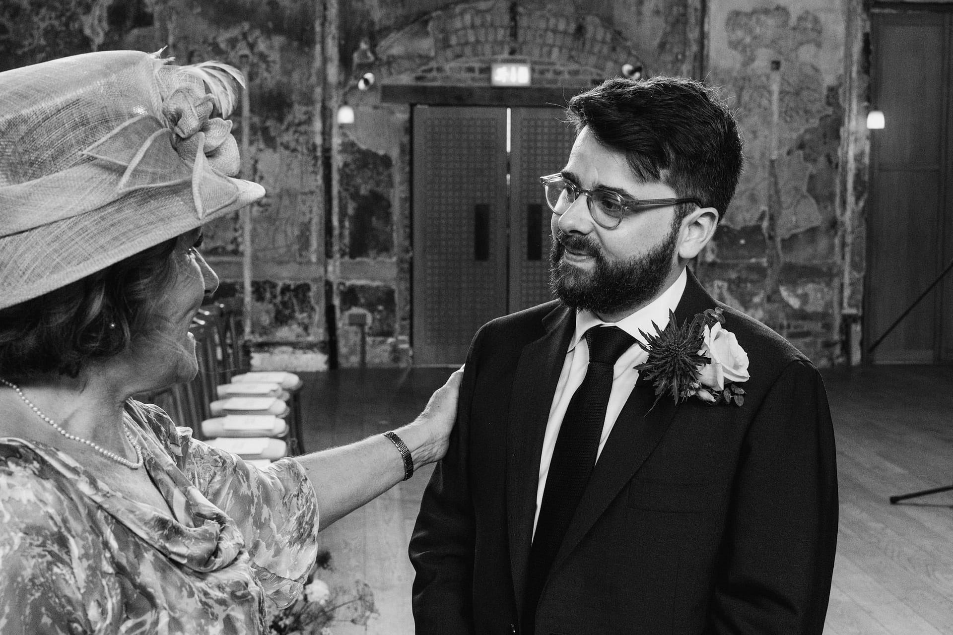 Elderly woman in hat congratulates groom at wedding.
