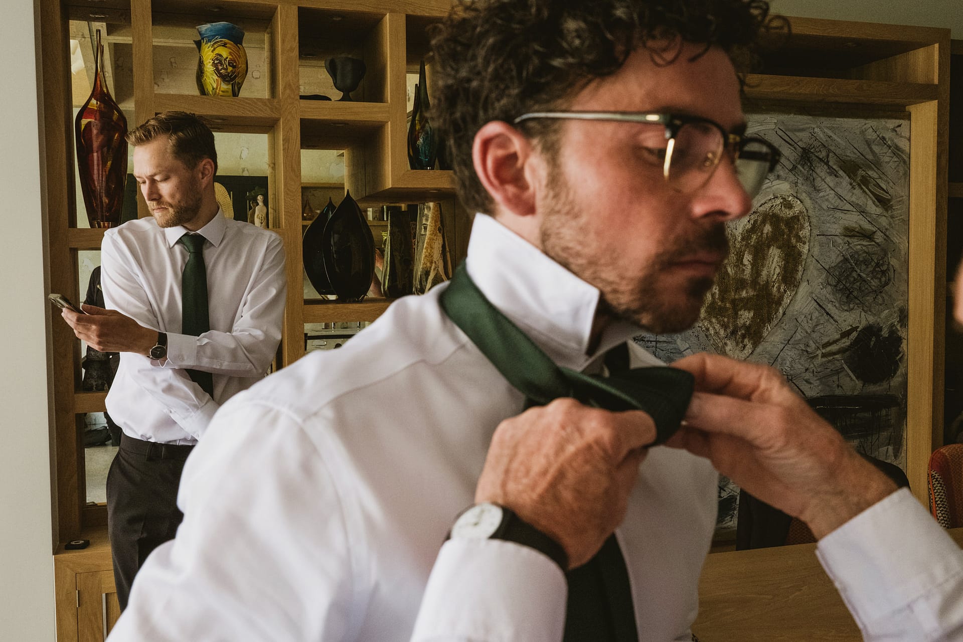Men preparing, tying ties in living room.