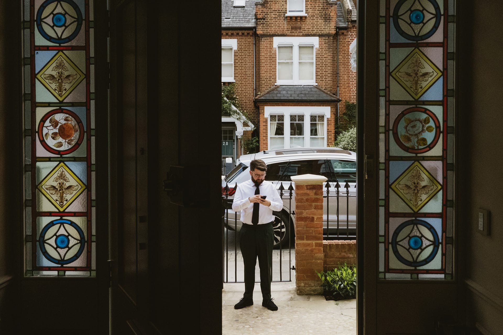 Man checking phone outside stained glass entrance.