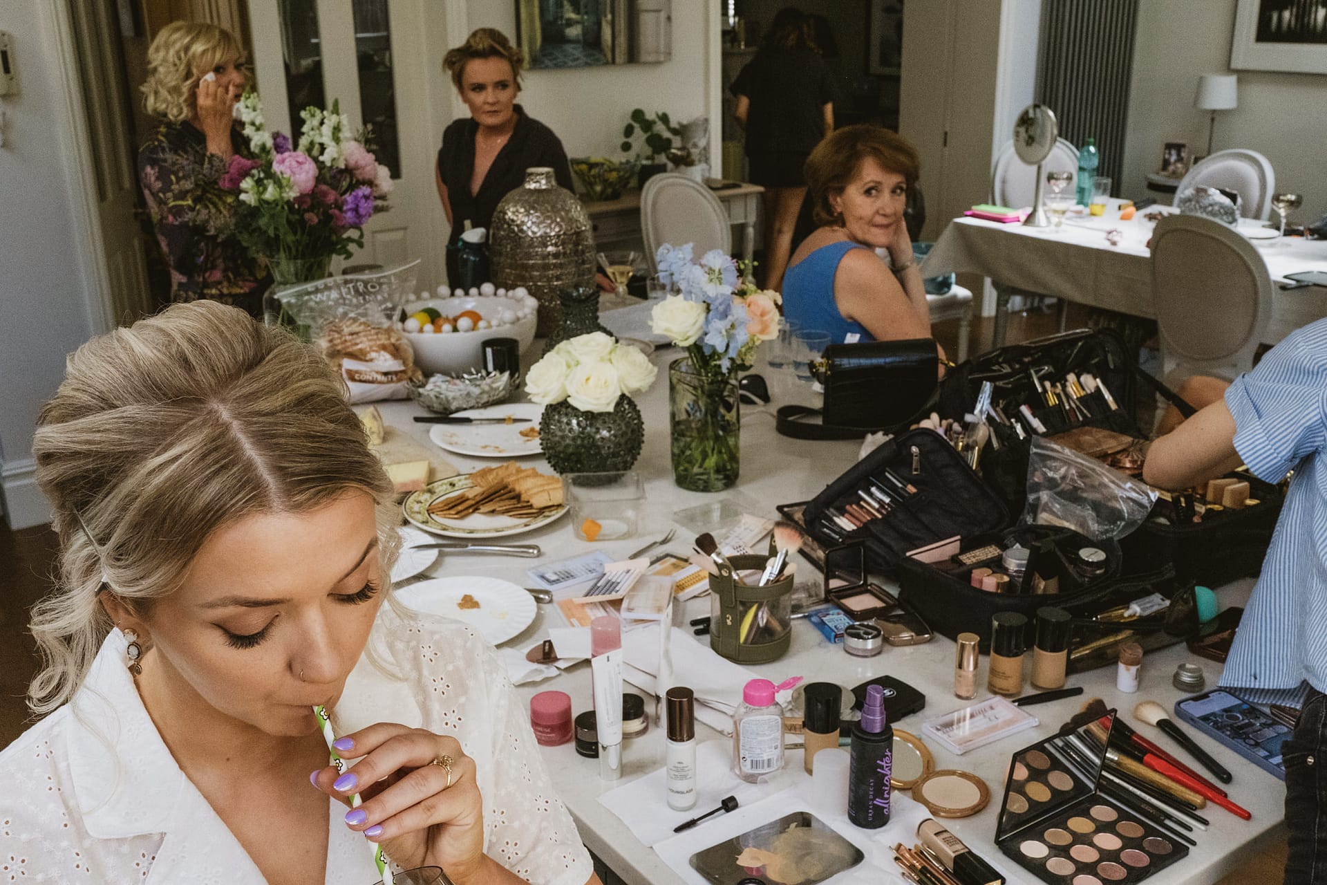 Women preparing for event with makeup and snacks.