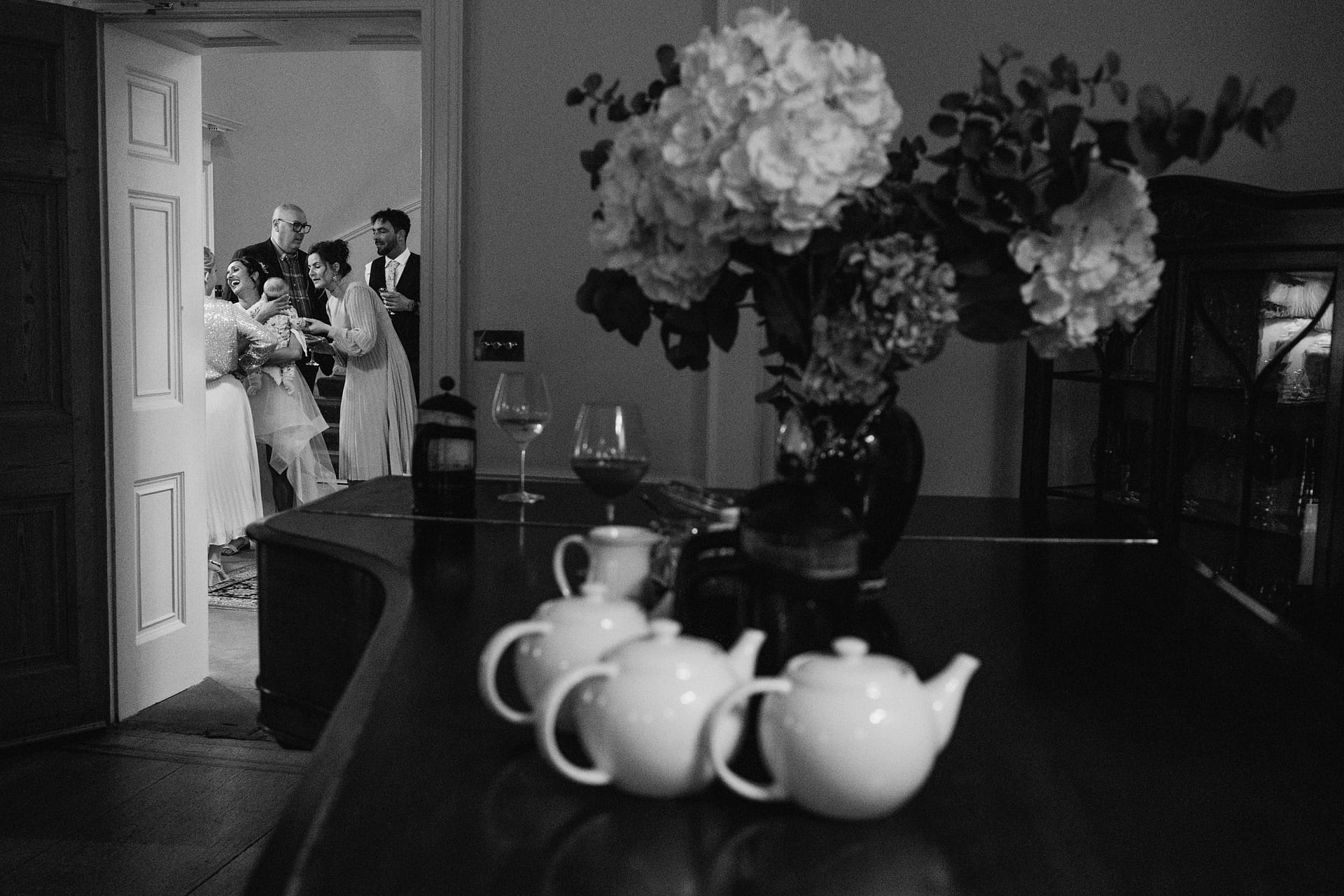Group celebrating near table with teapots and flowers.