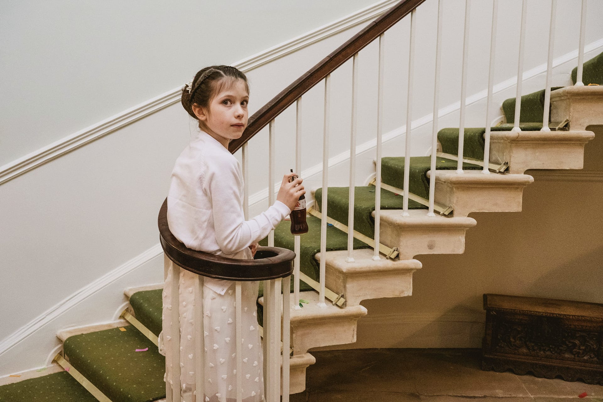 Girl holding bottle on green-carpeted staircase