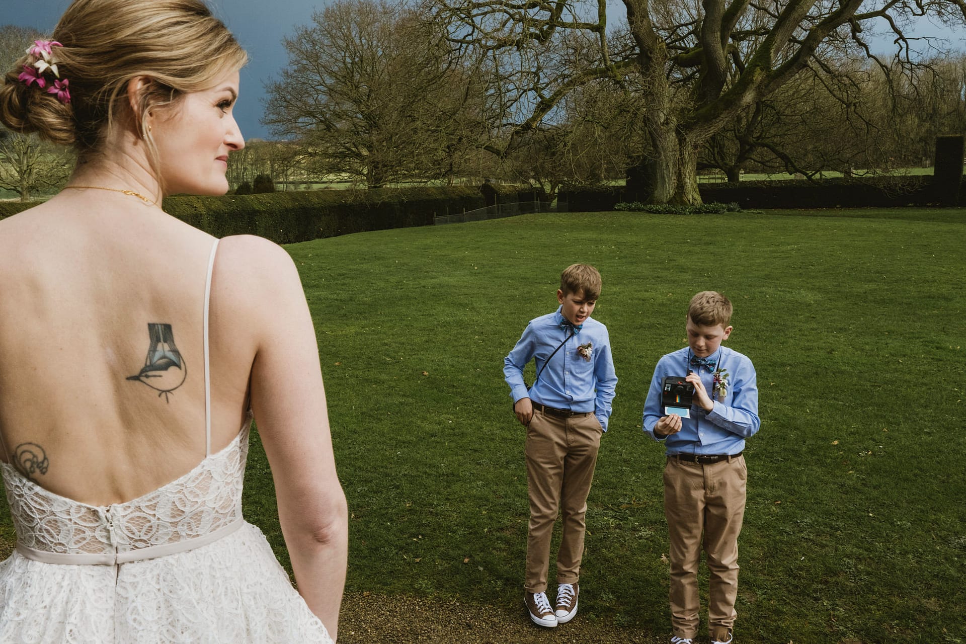 Bride with tattoo, boys taking photo in garden.