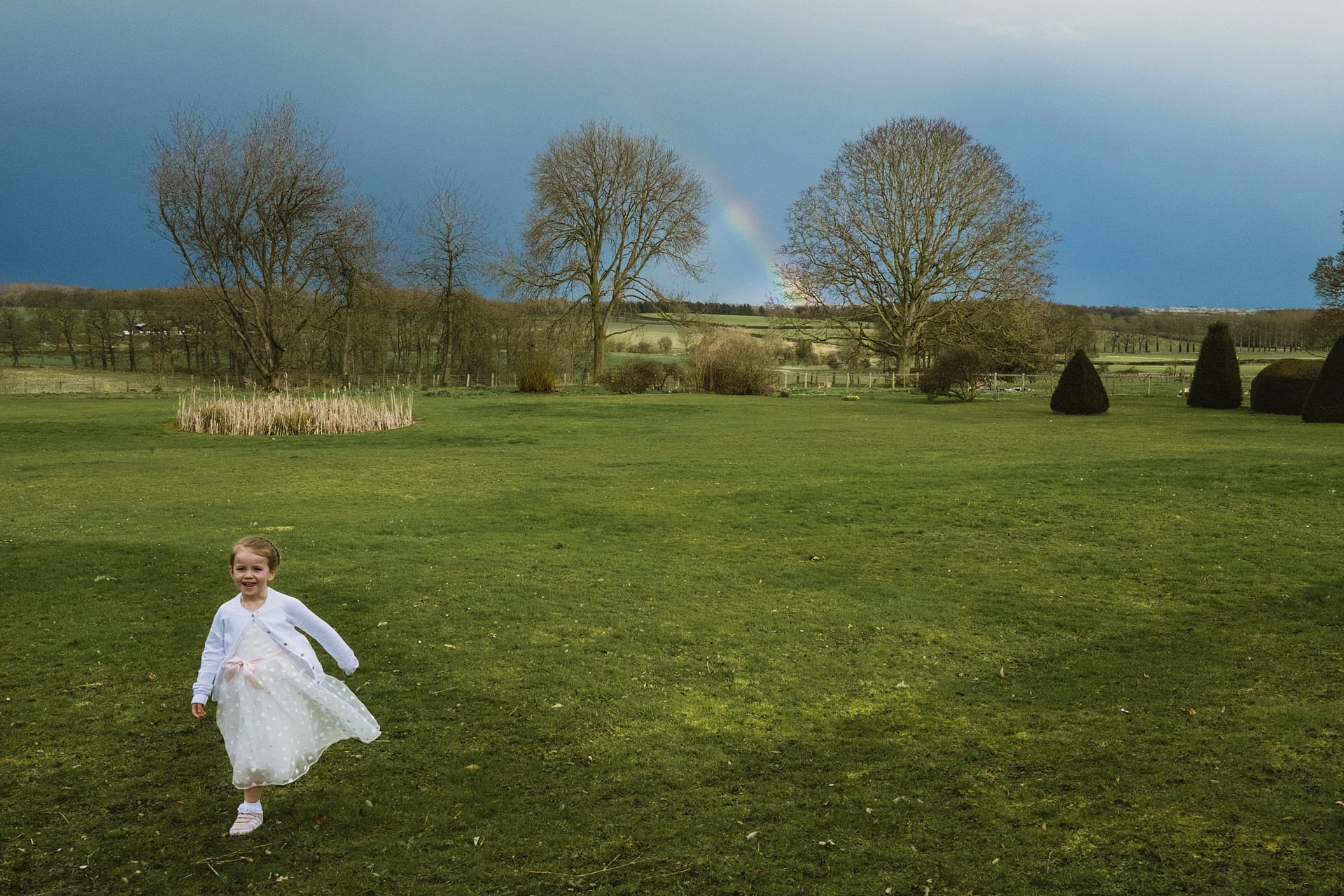 Child running on green field with rainbow backdrop.