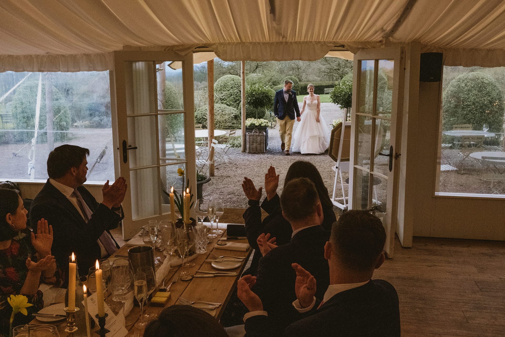 Bride and groom enter wedding reception, guests applauding.