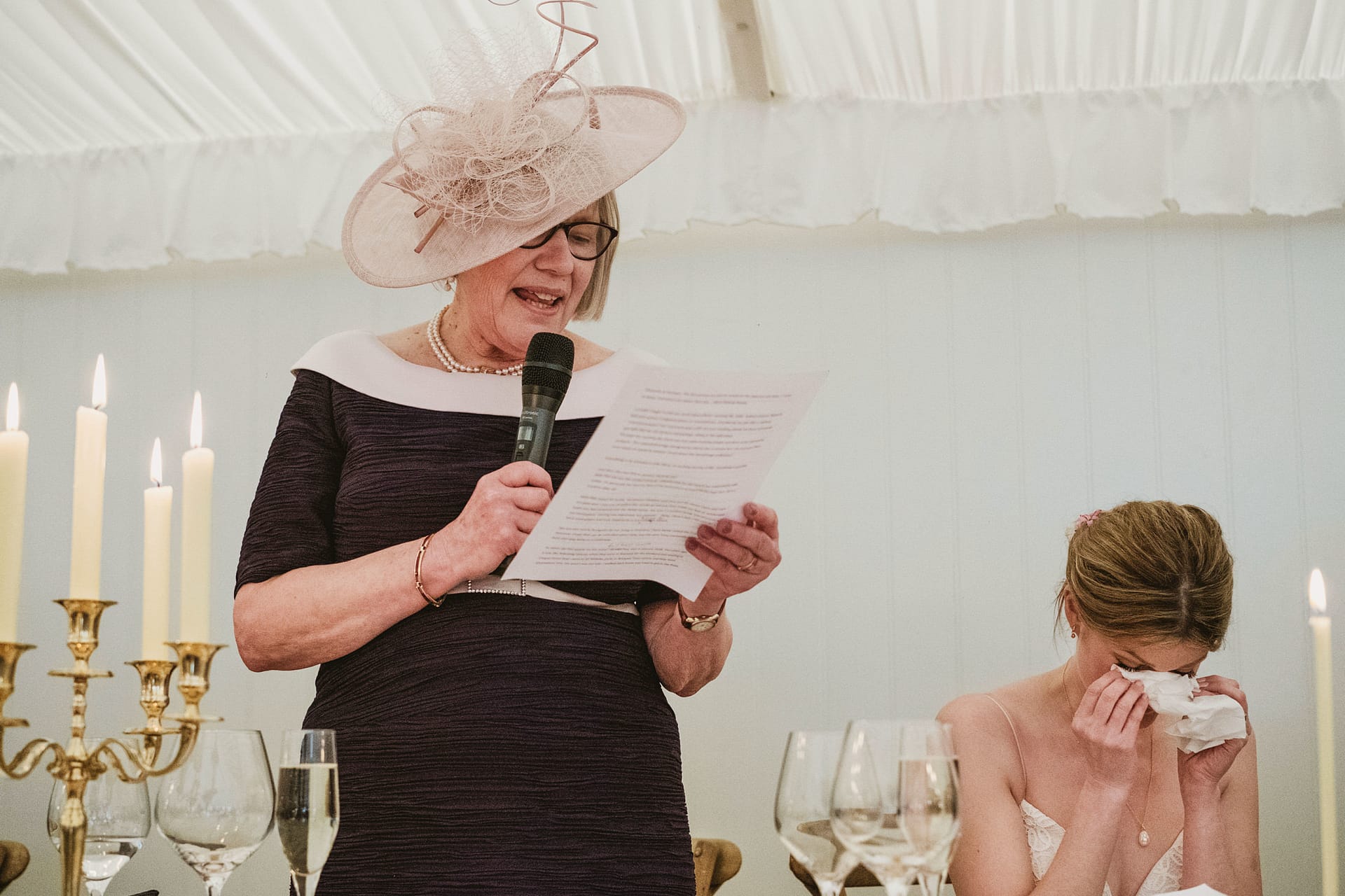 Woman giving speech, bride wipes tears at wedding.