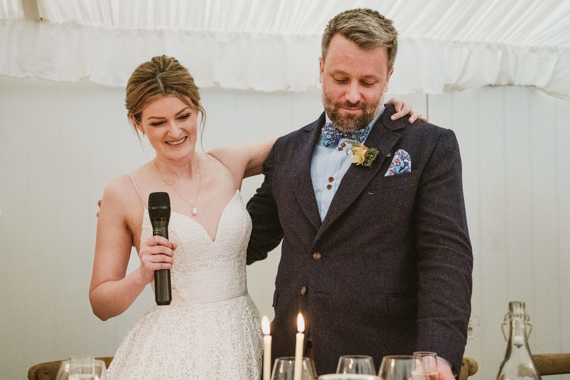 Bride giving wedding speech with groom smiling.