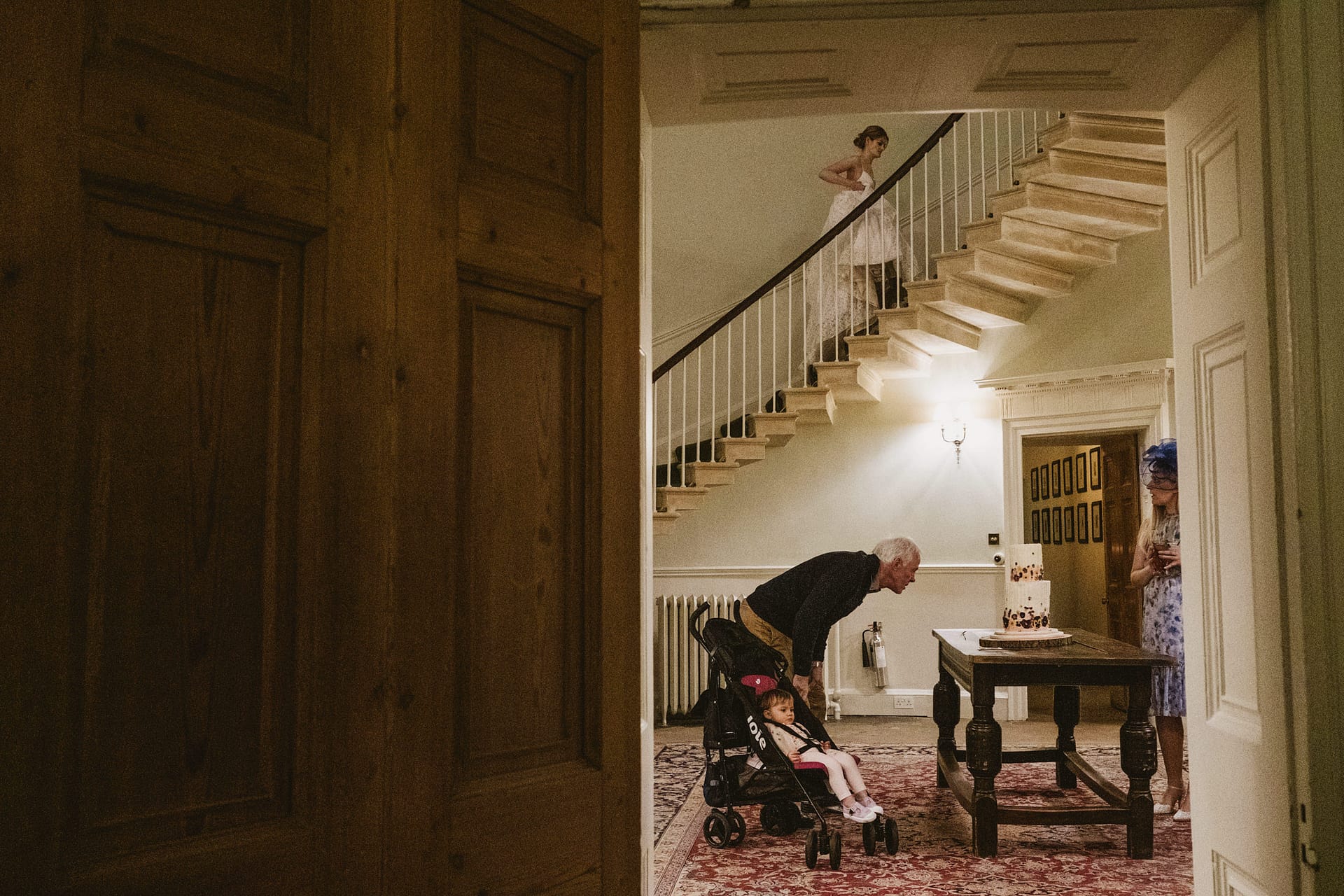 Man with stroller, woman descending staircase, cake on table.