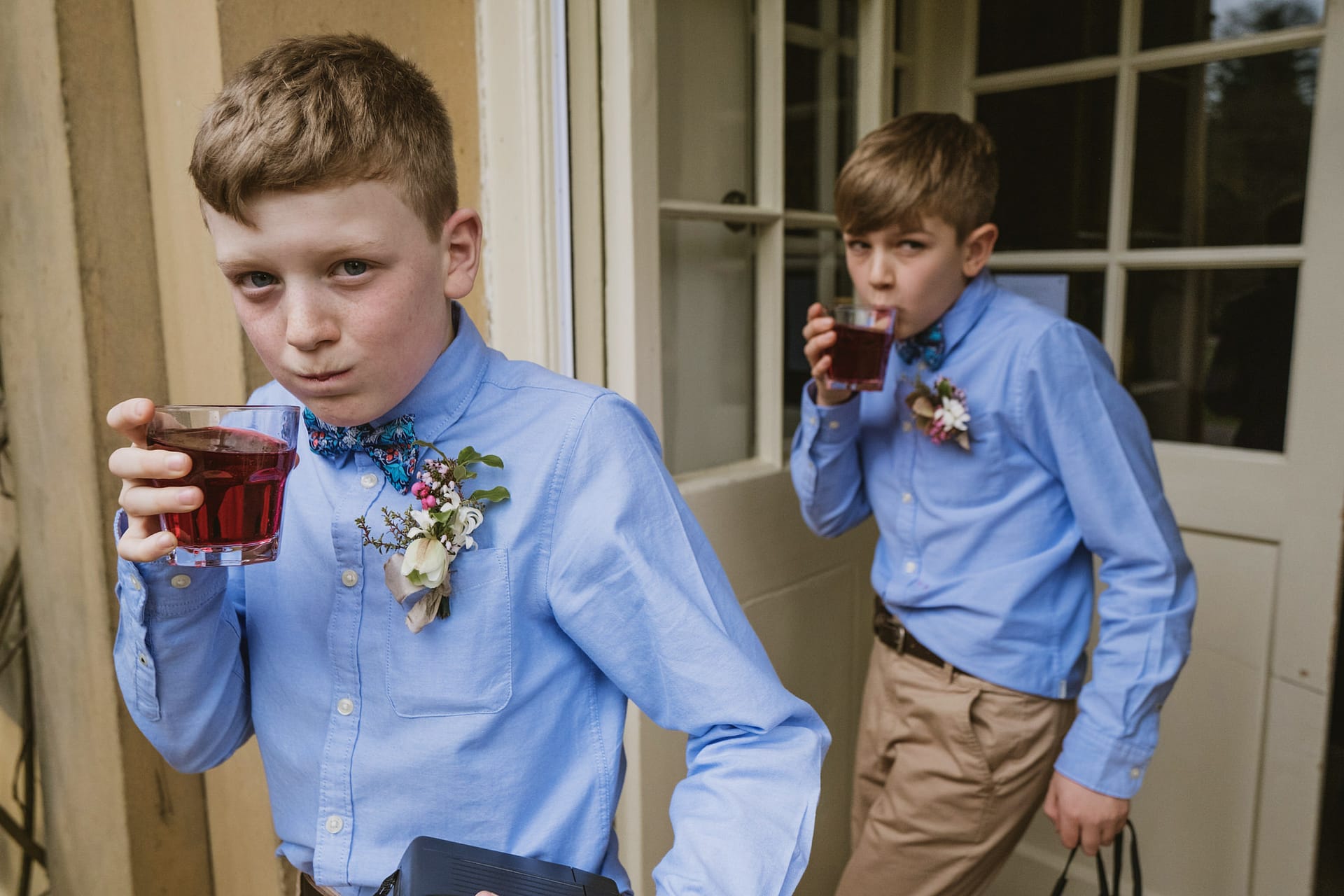 Boys in blue shirts drink red juice at event.