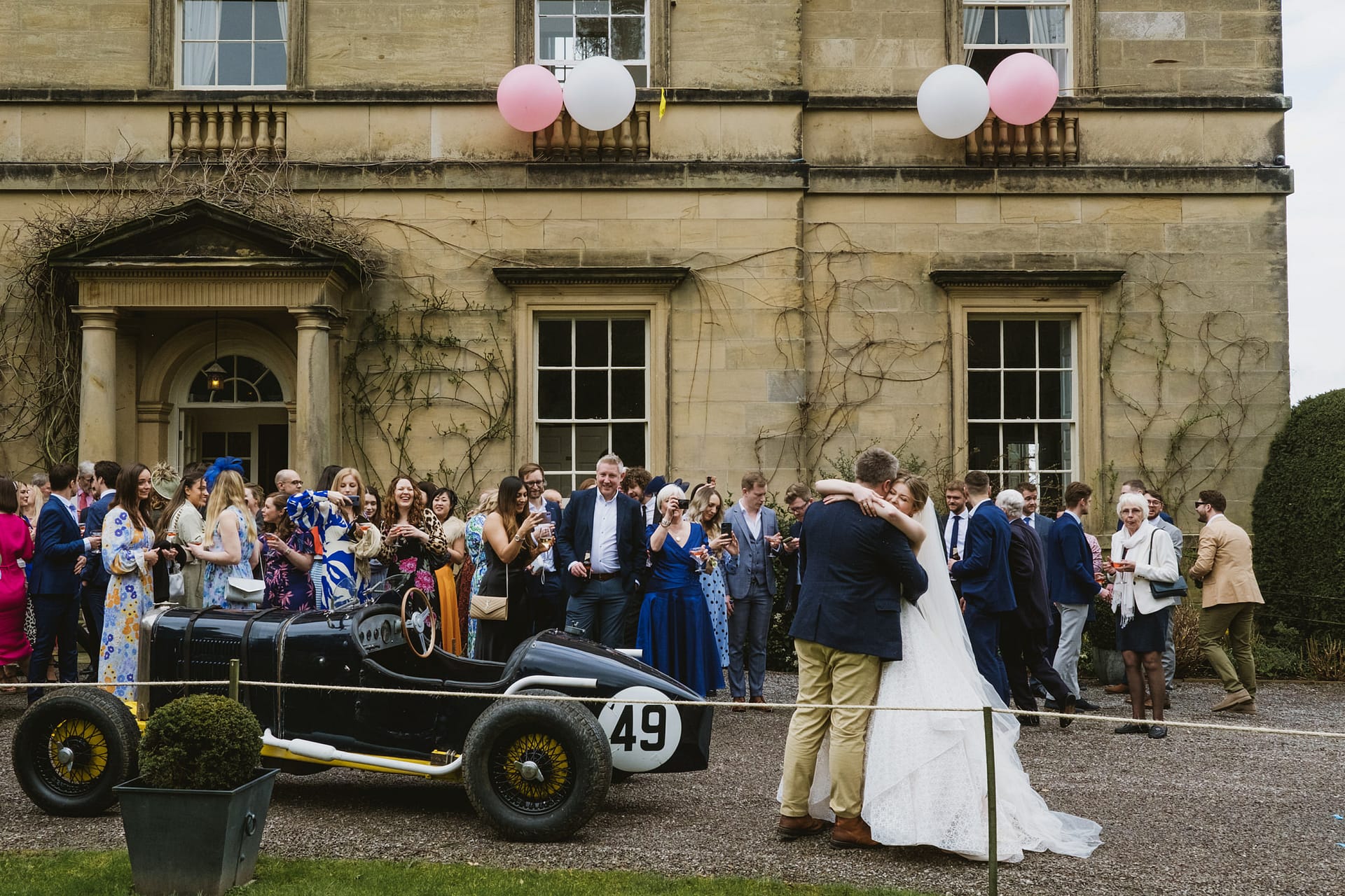 Wedding guests gathered outside vintage building with balloons.