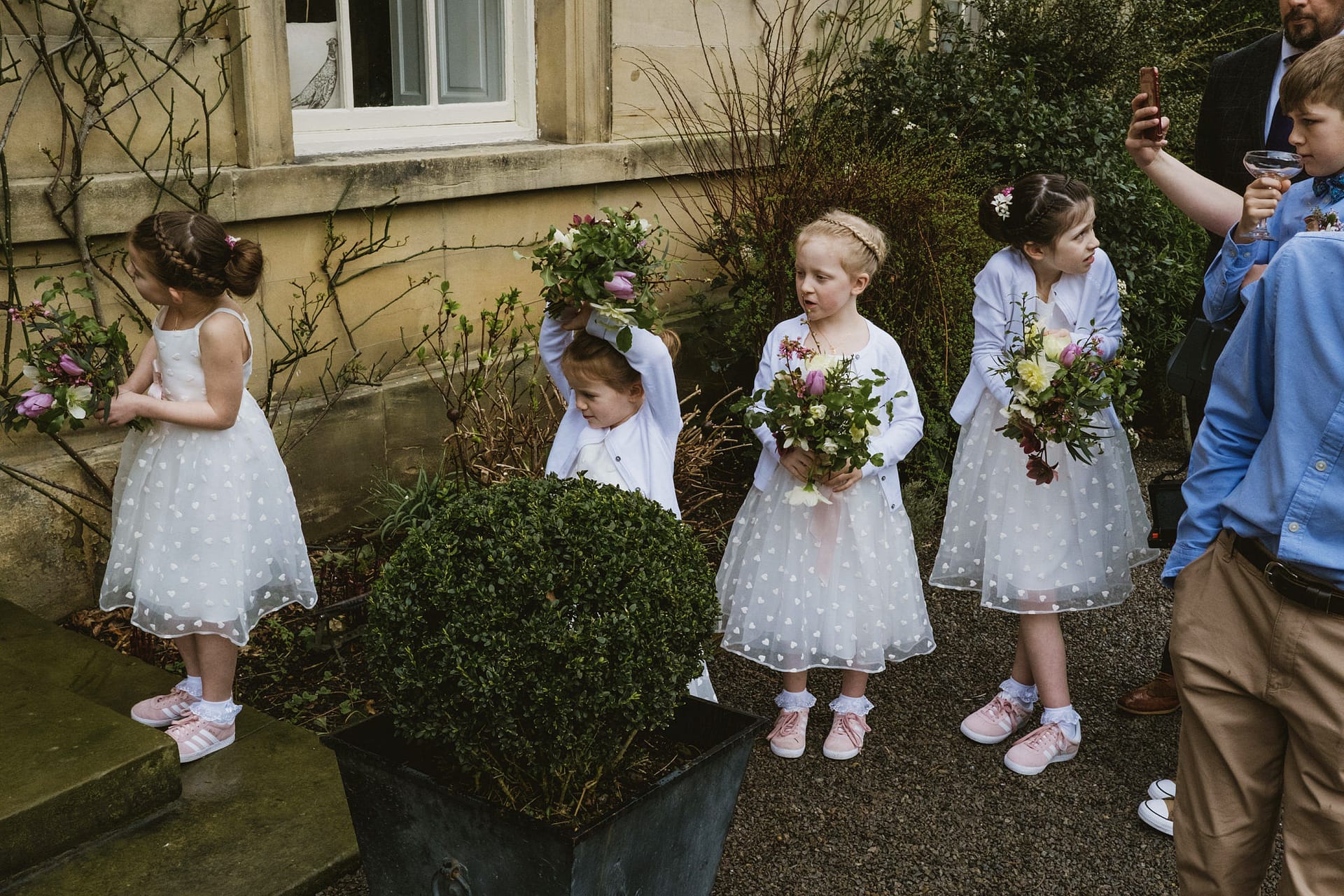 Children in white dresses holding flower bouquets, outside.