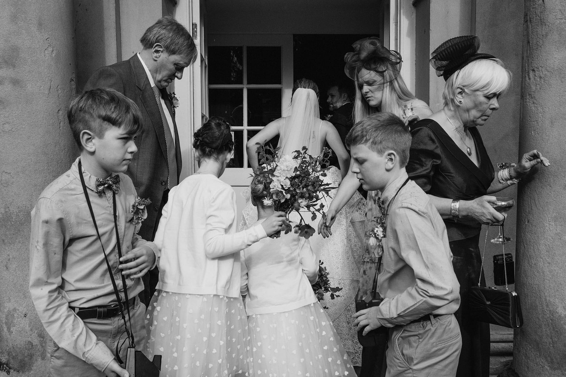 Wedding guests enter venue, holding flowers, dressed formally.