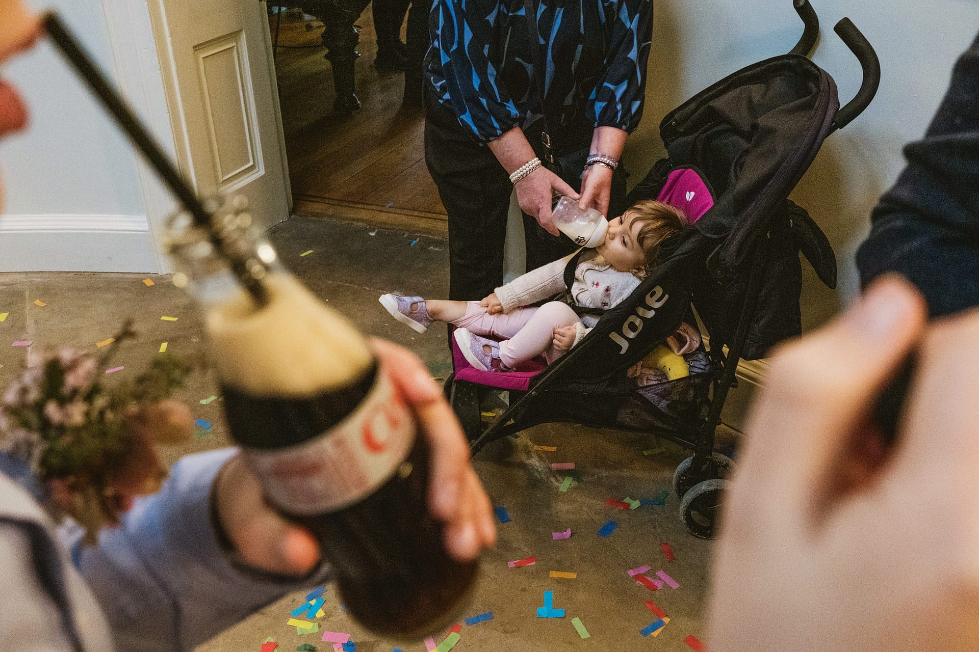 Toddler in buggy drinking milk bottle, surrounded by confetti.
