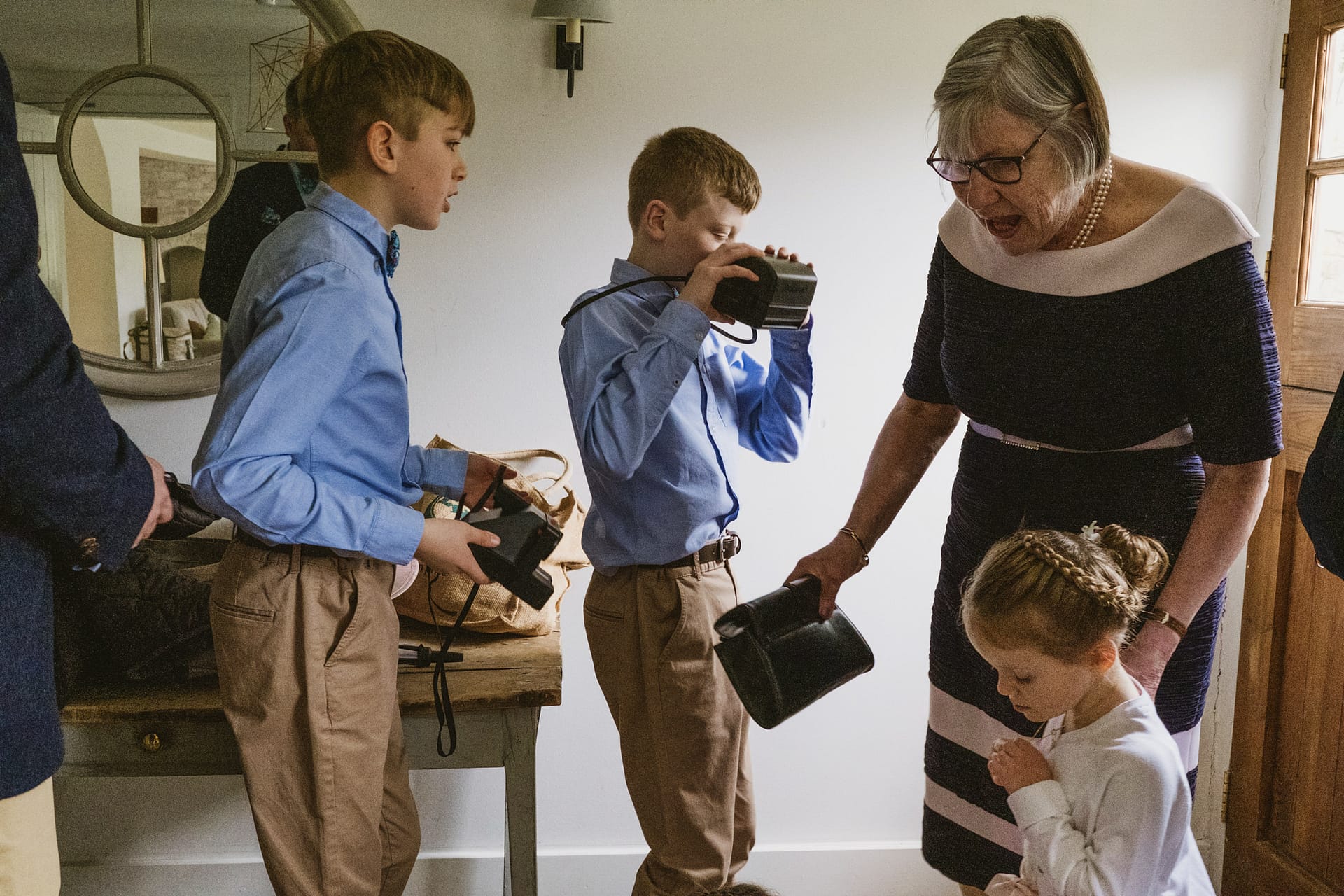 Children exploring cameras with an older woman indoors.