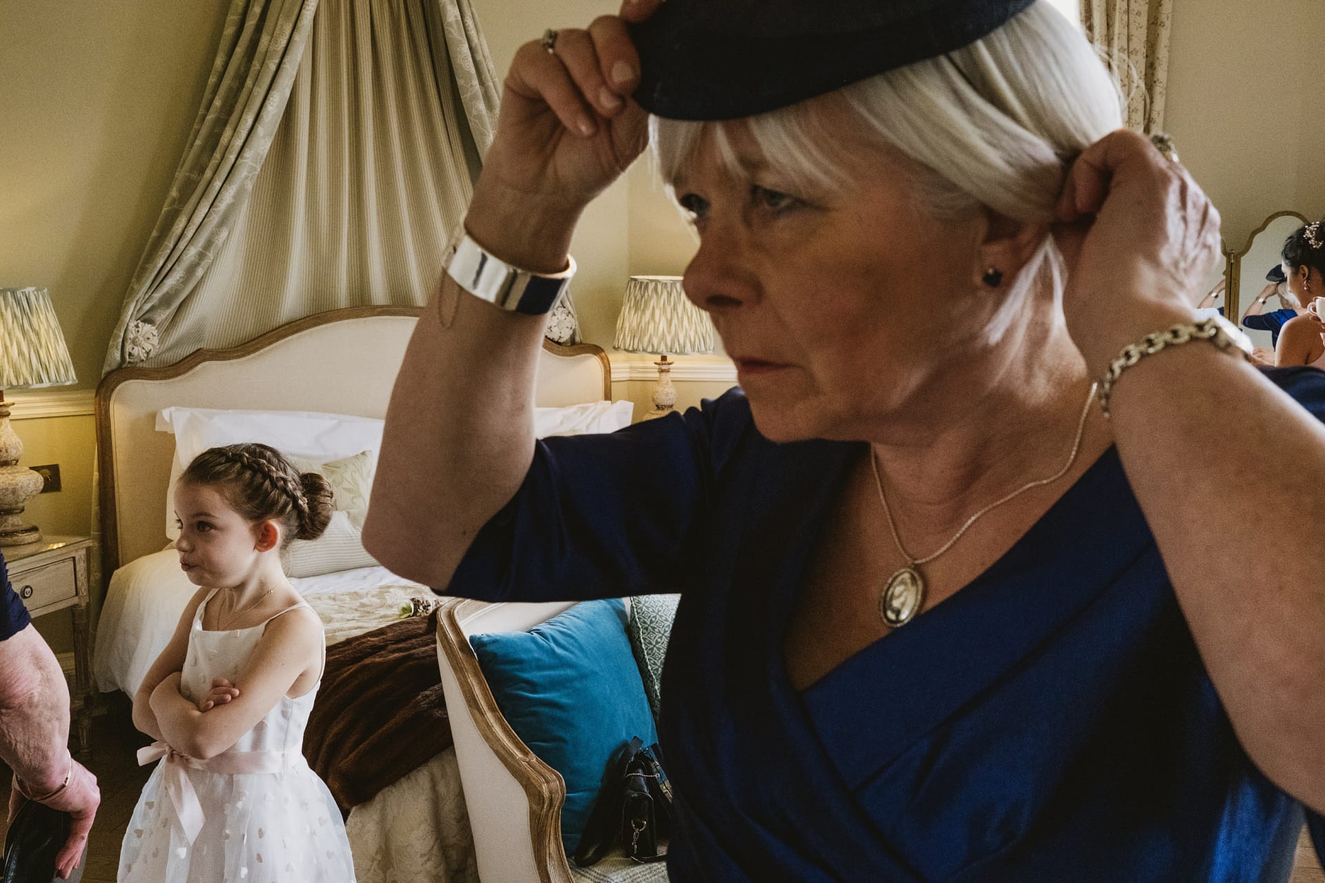 Woman adjusting hat, child in background, elegant room