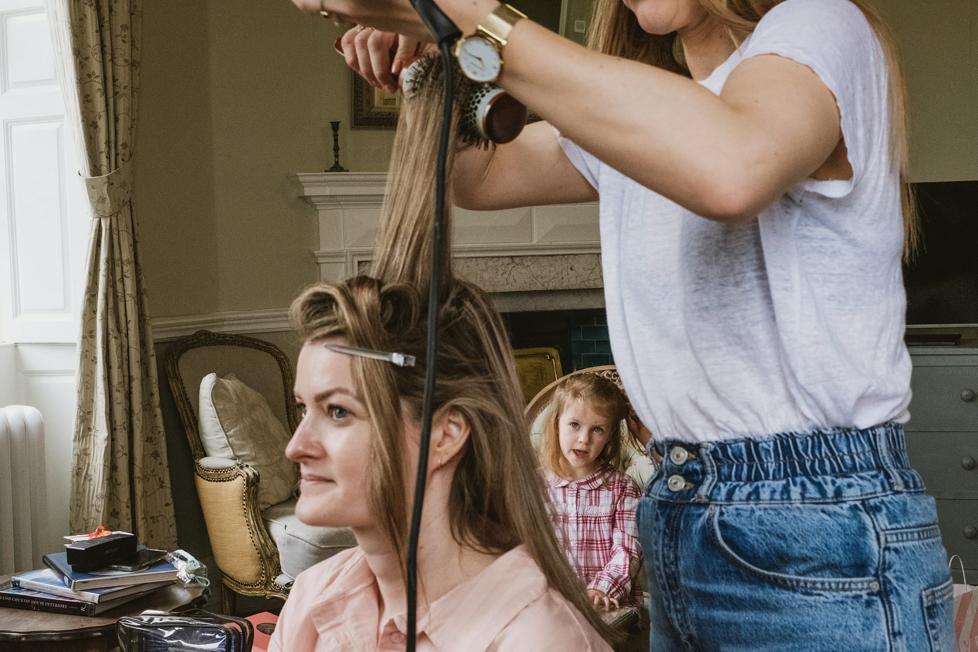 Hair stylist curling woman's hair at home.