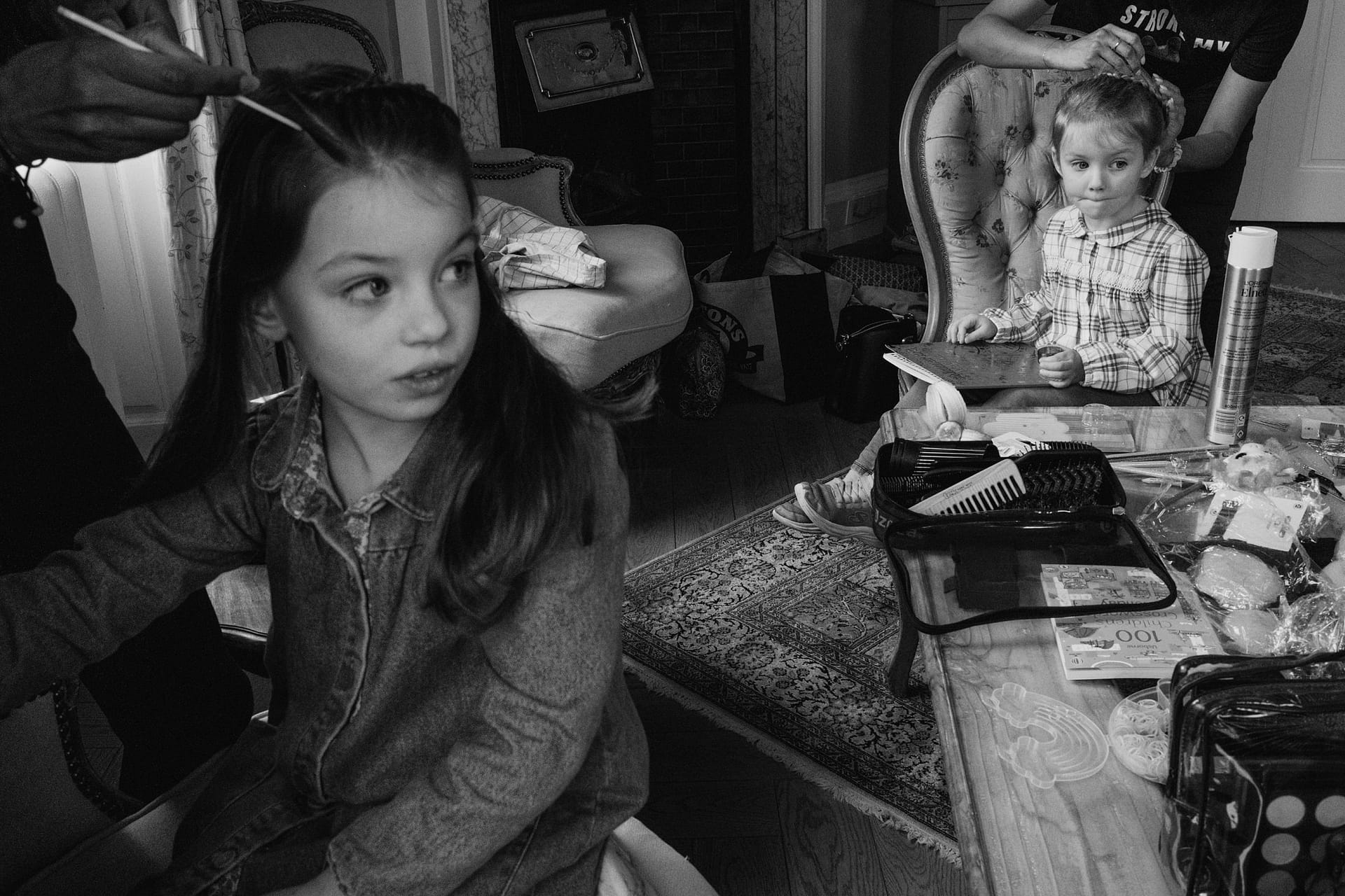 Children getting hair styled in living room setting.