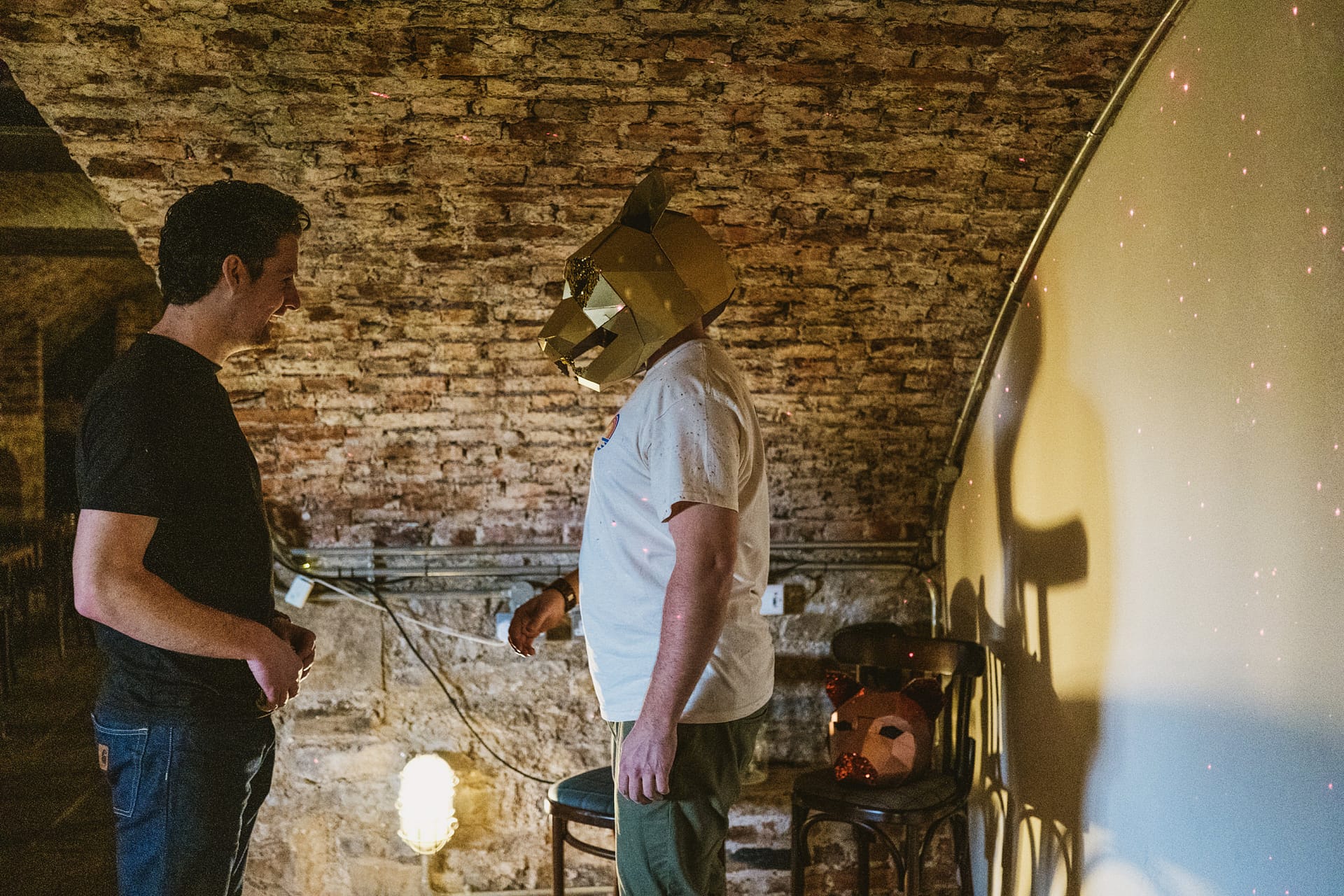 Man wearing geometric lion mask faces another man.
