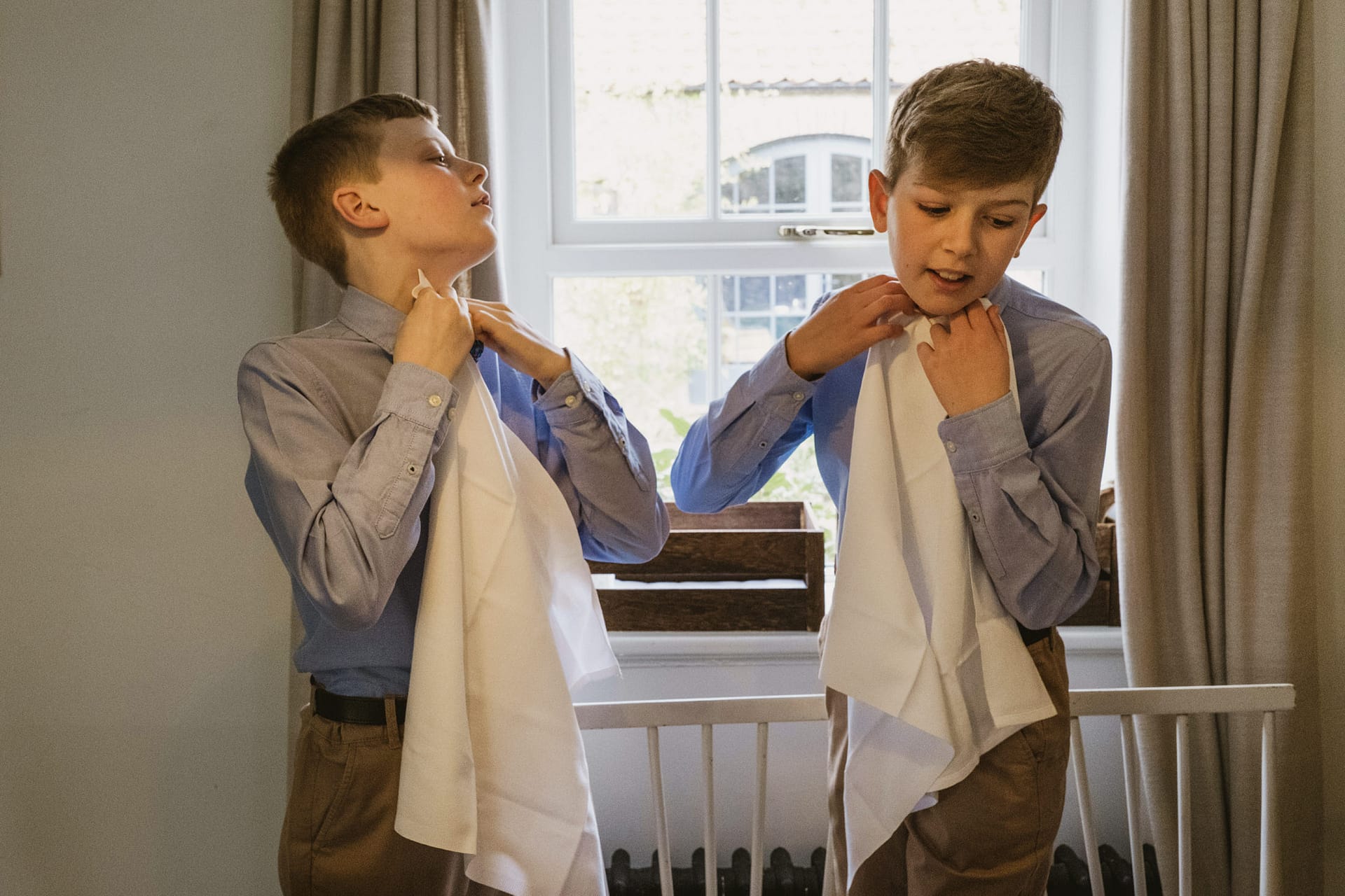 Two boys tying bow ties in bedroom.
