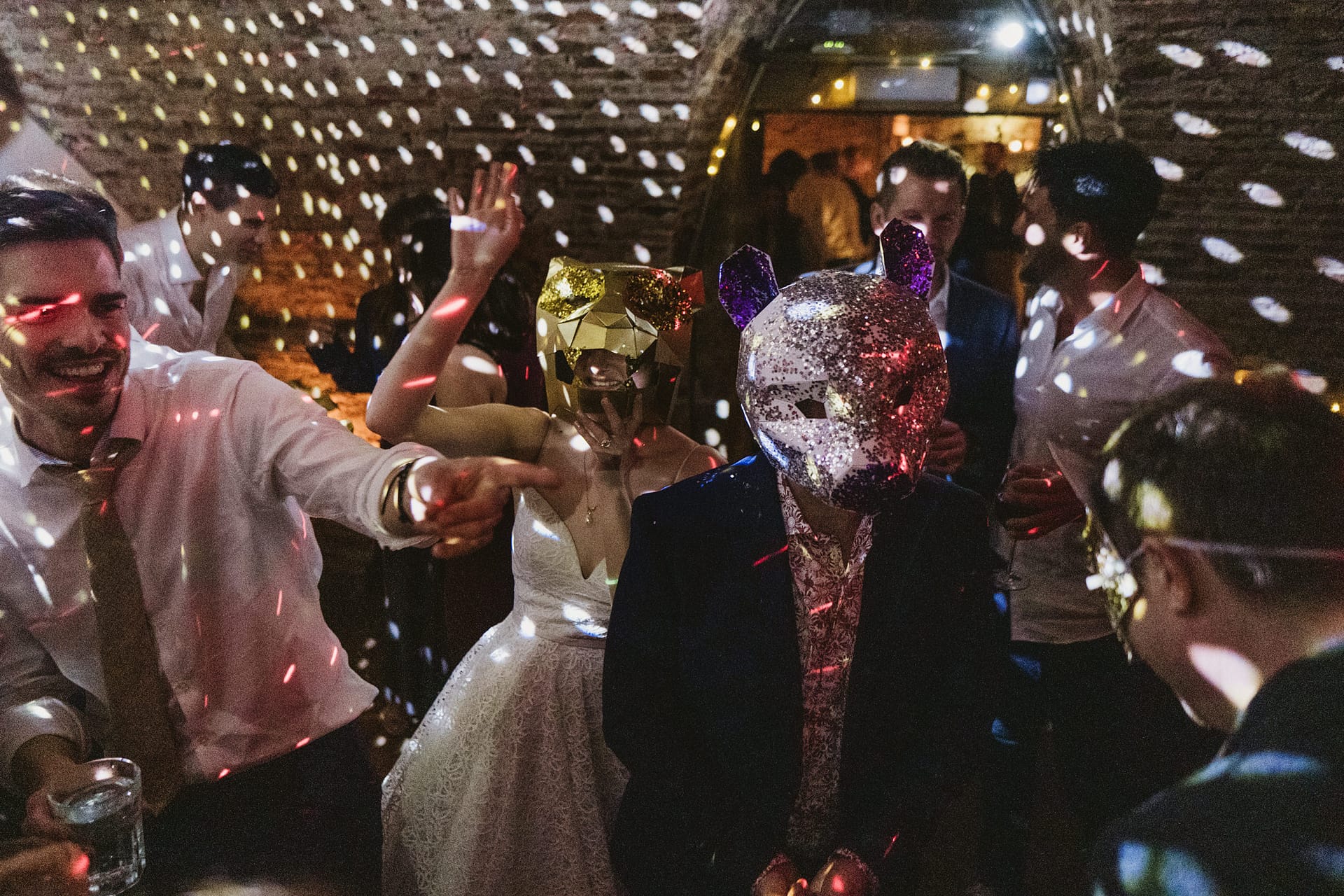 Masked wedding guests dancing under disco lights.