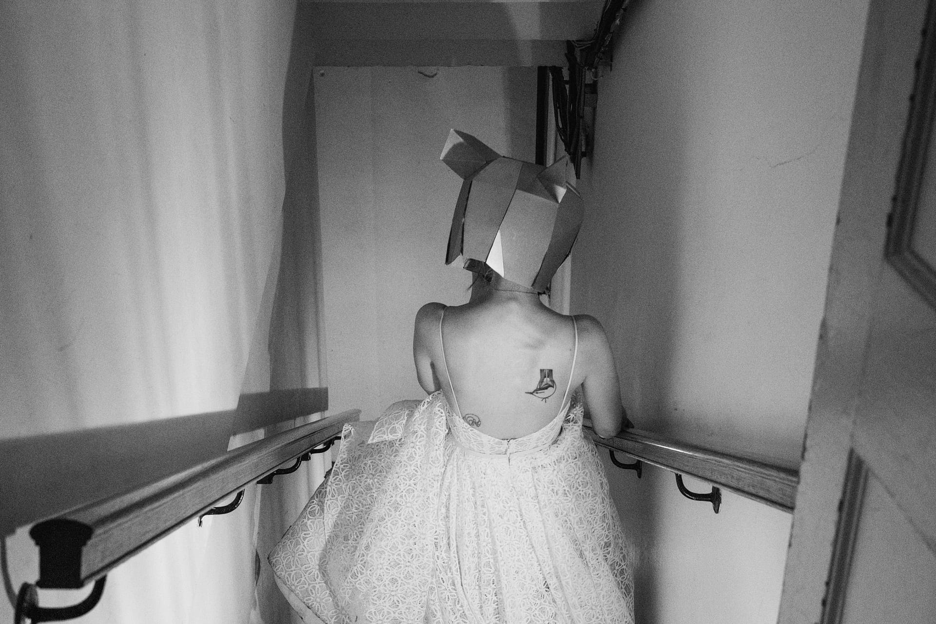 Woman in dress with paper hat and tattoo walking downstairs.