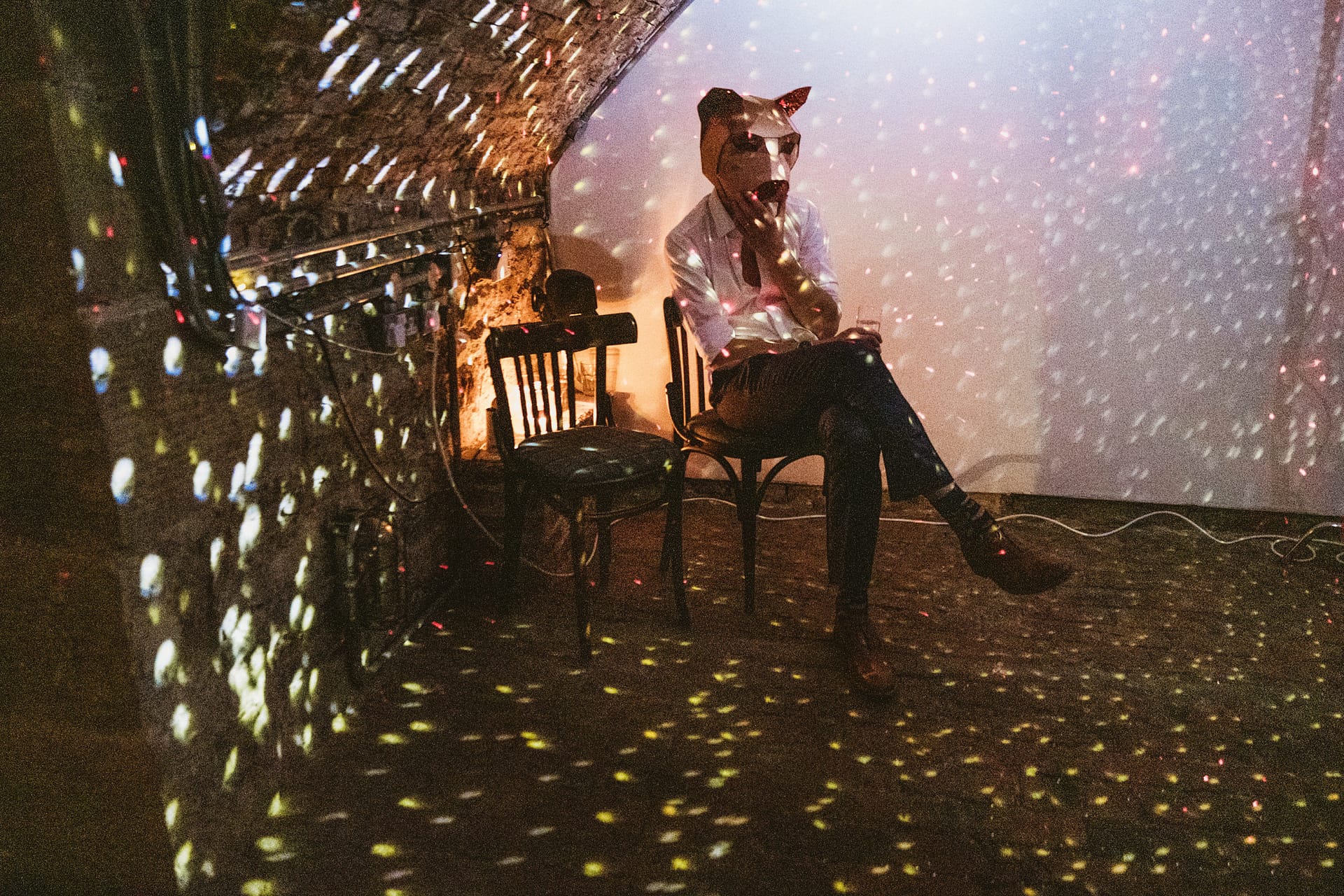 Person in fox mask sitting under disco lights.