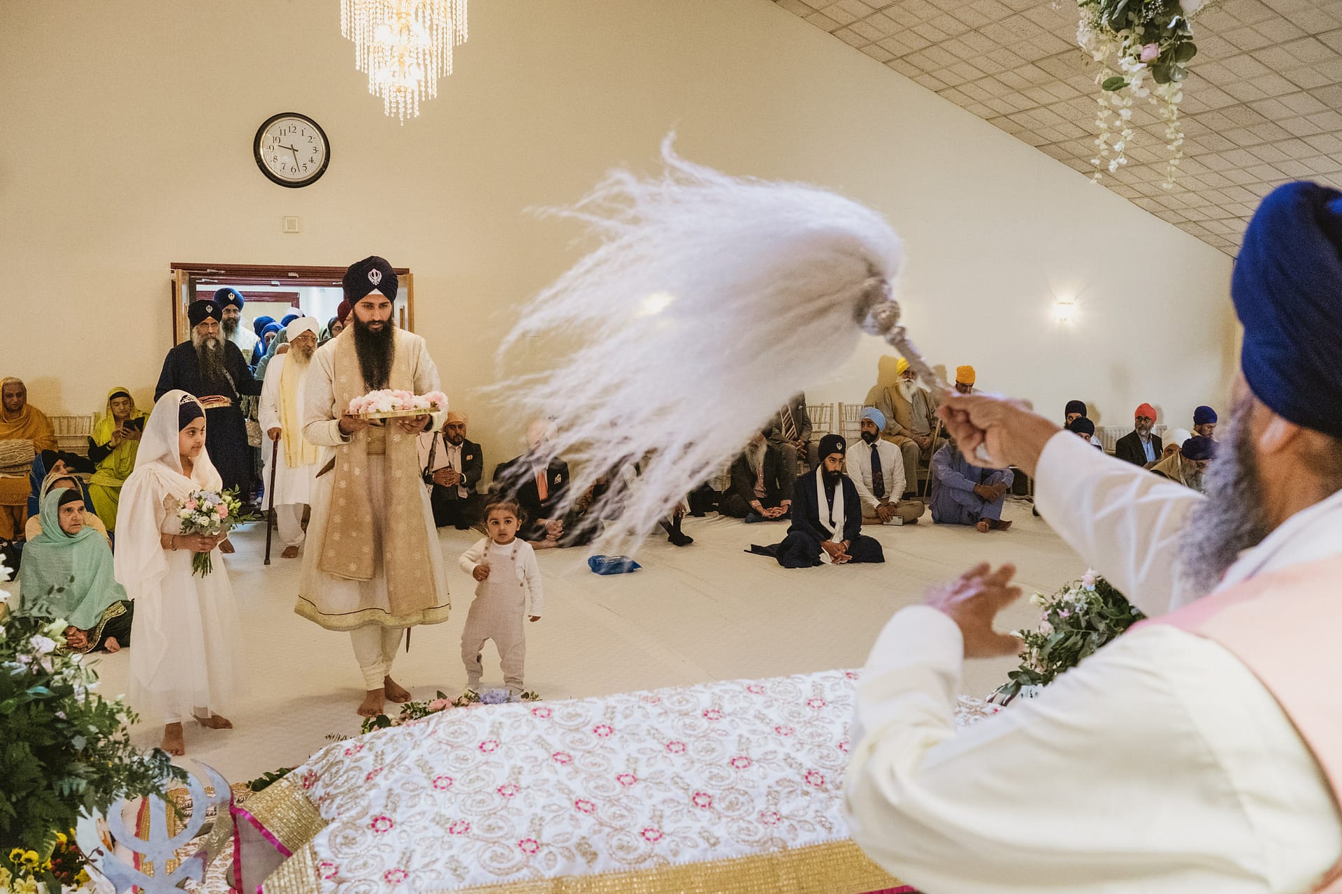 Sikh wedding ceremony with attendees and ritual objects.