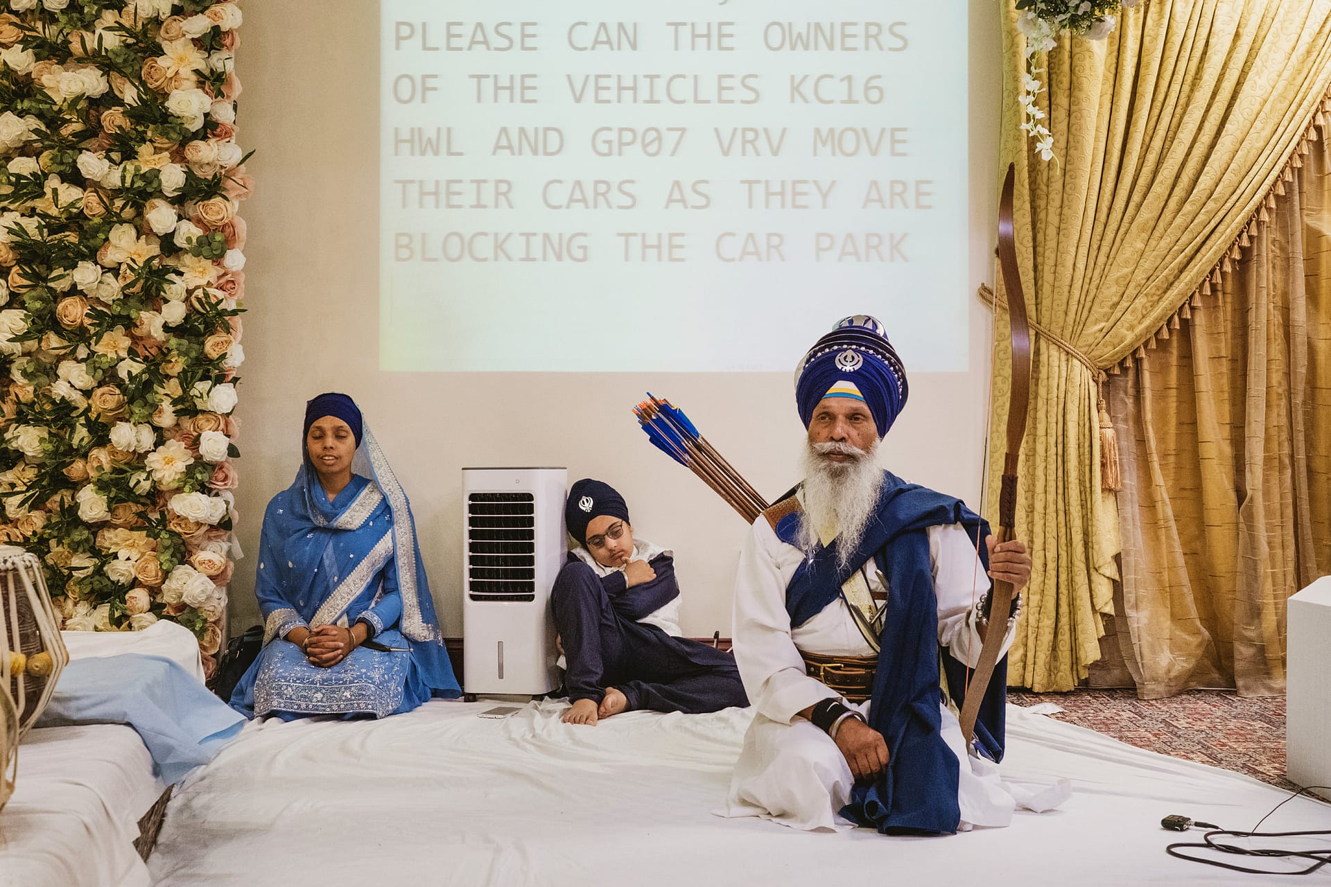 Sikh congregation with projection screen notice behind.