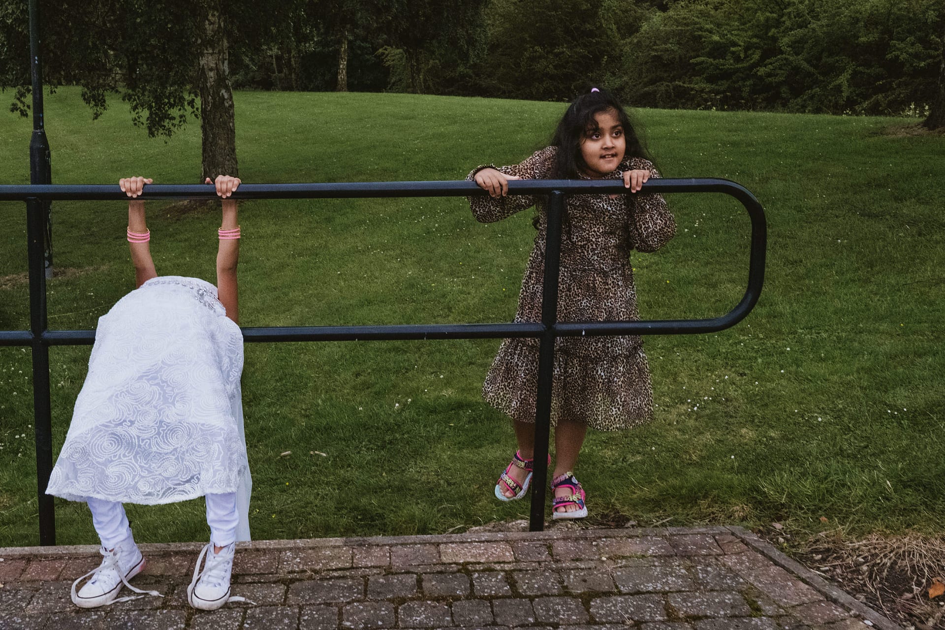 Children playing on park railings, grassy field behind.