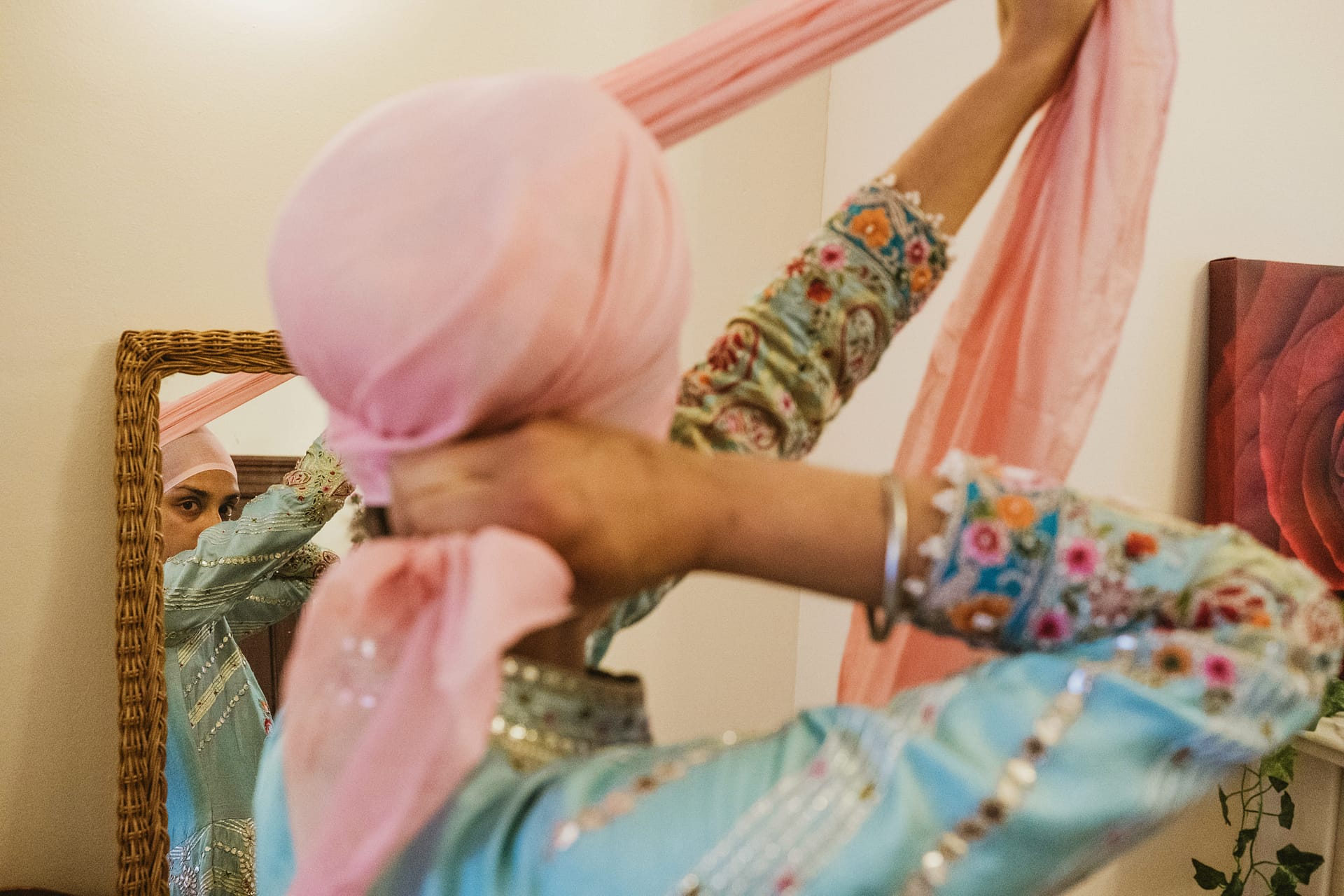 Person tying pink turban in front of mirror.
