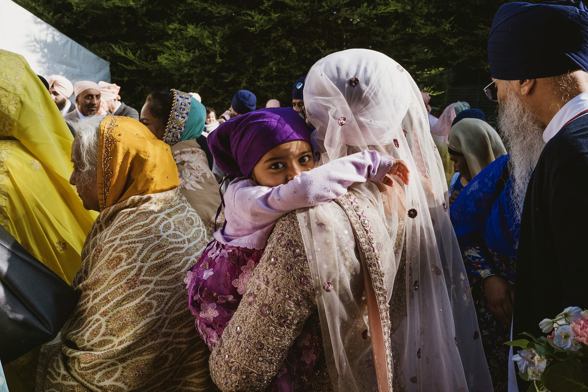 Child in purple turban hugging woman at gathering.