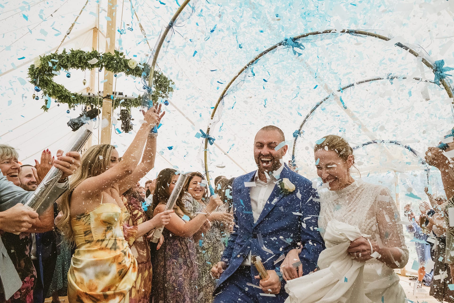 Wedding couple under confetti shower with guests cheering.